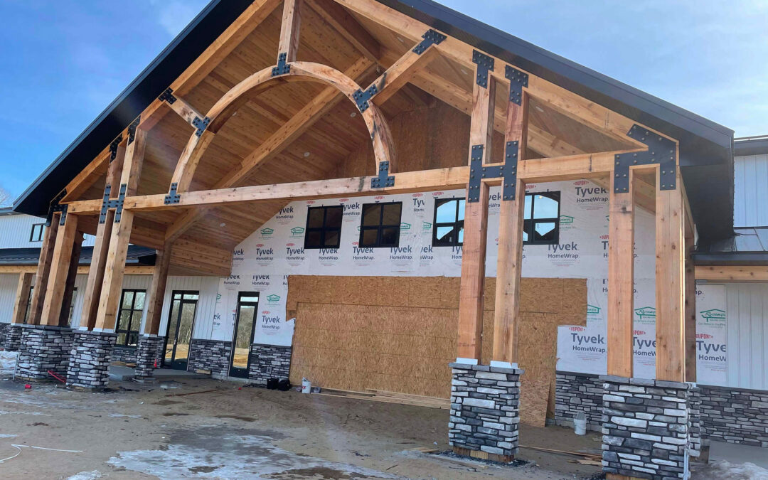 Martin's Truss Manufacturing Elkhart IN A partially constructed building with exposed wooden beams, stone pillars, and Tyvek wrap on the exterior walls; large entryway is boarded up.