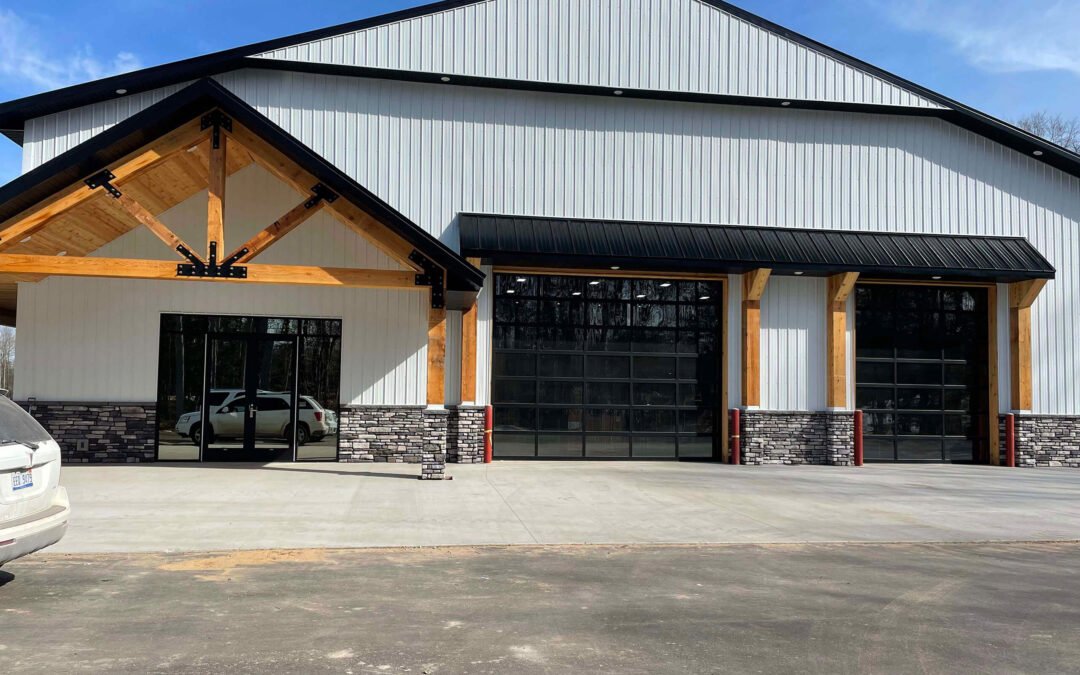 Martin's Truss Manufacturing Elkhart IN A large modern building with metal siding, glass garage doors, and stone accents; vehicles are parked outside on a paved surface.