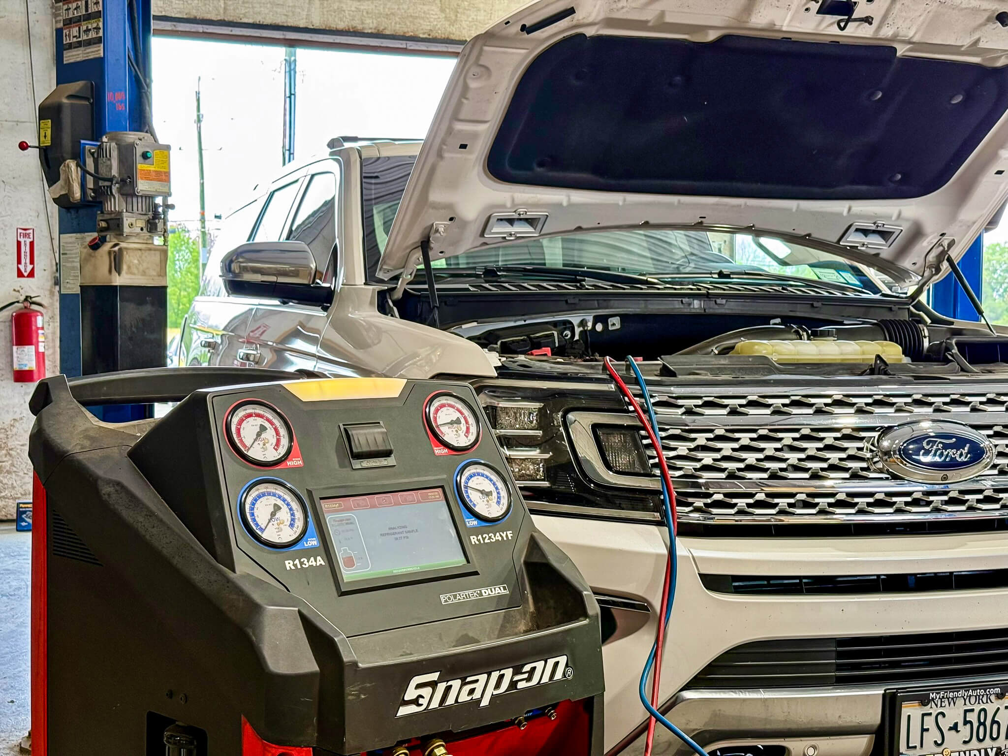 A white Ford SUV with its hood open is connected to a Snap-on diagnostic machine in an auto repair shop.