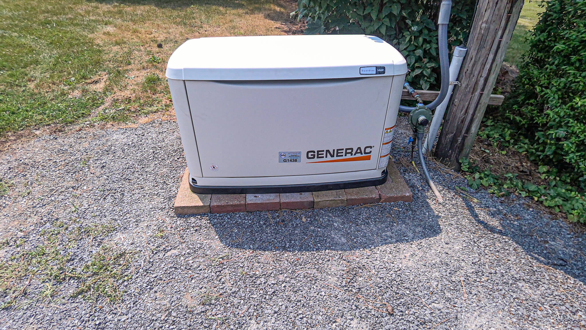 A Generac standby generator is installed outdoors on a base of bricks and gravel, next to a utility pole and electrical connections.