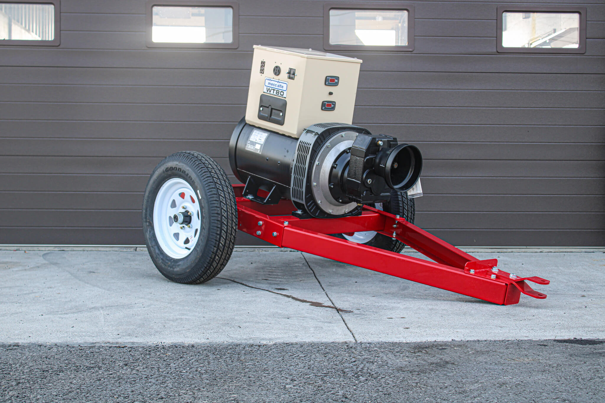 A portable industrial fan or blower on a red wheeled frame, positioned outdoors in front of a brown garage door.