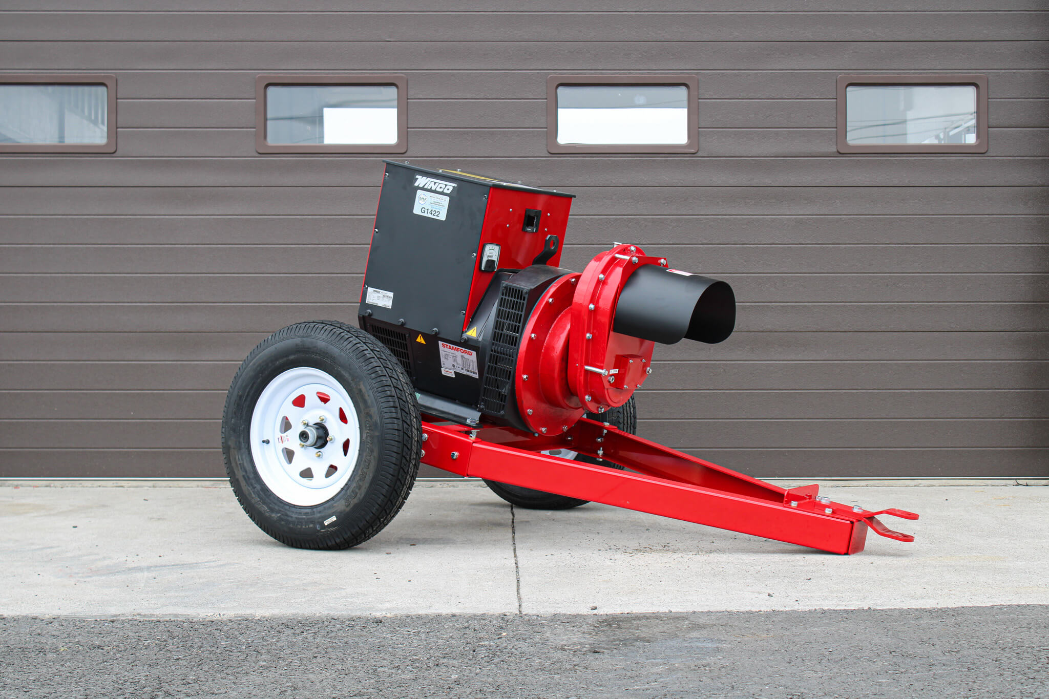 Red and black industrial leaf blower on wheels is positioned on concrete in front of a brown garage door.