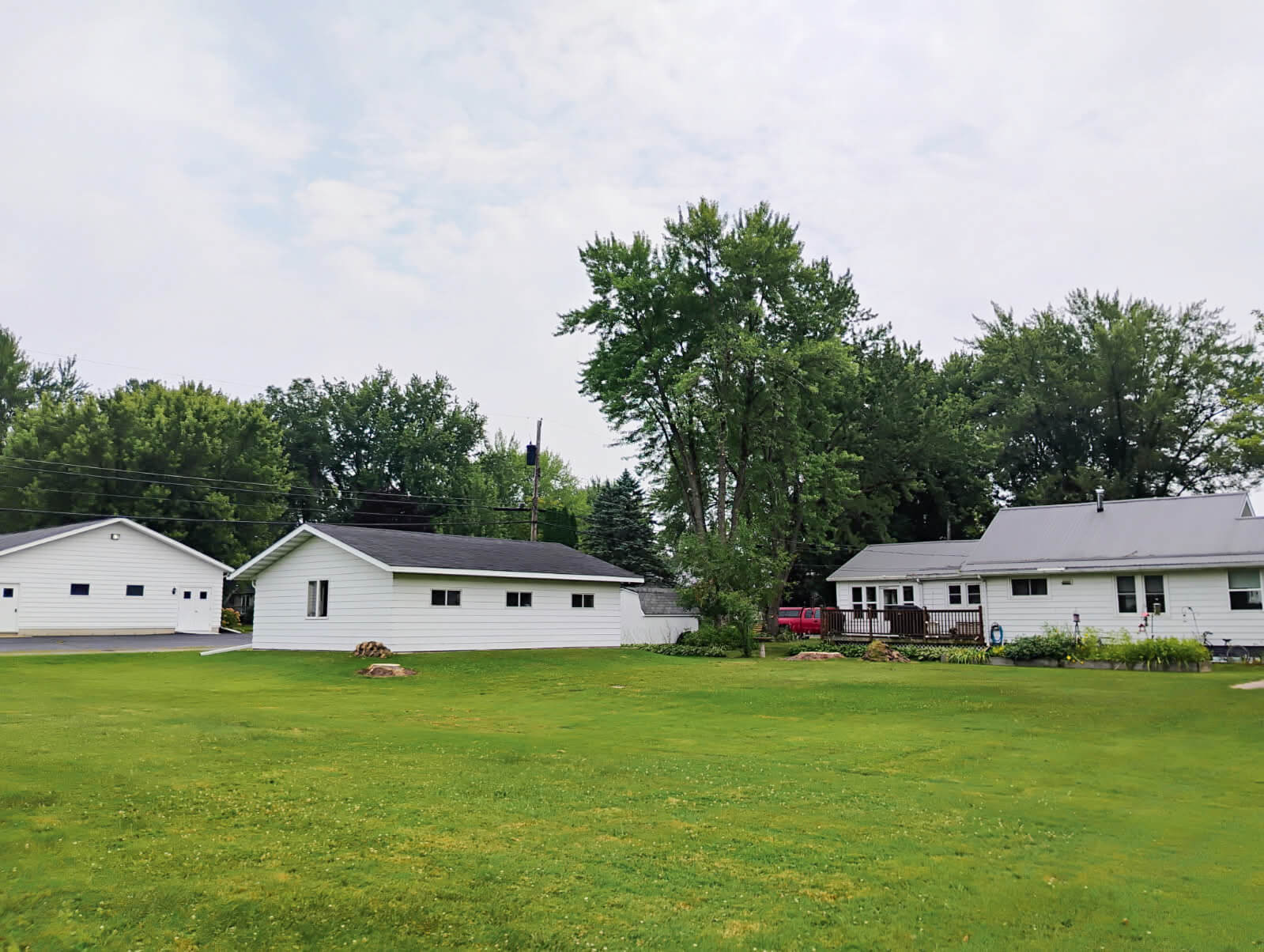 Large grassy yard with two white single-story buildings and several trees under a cloudy sky.