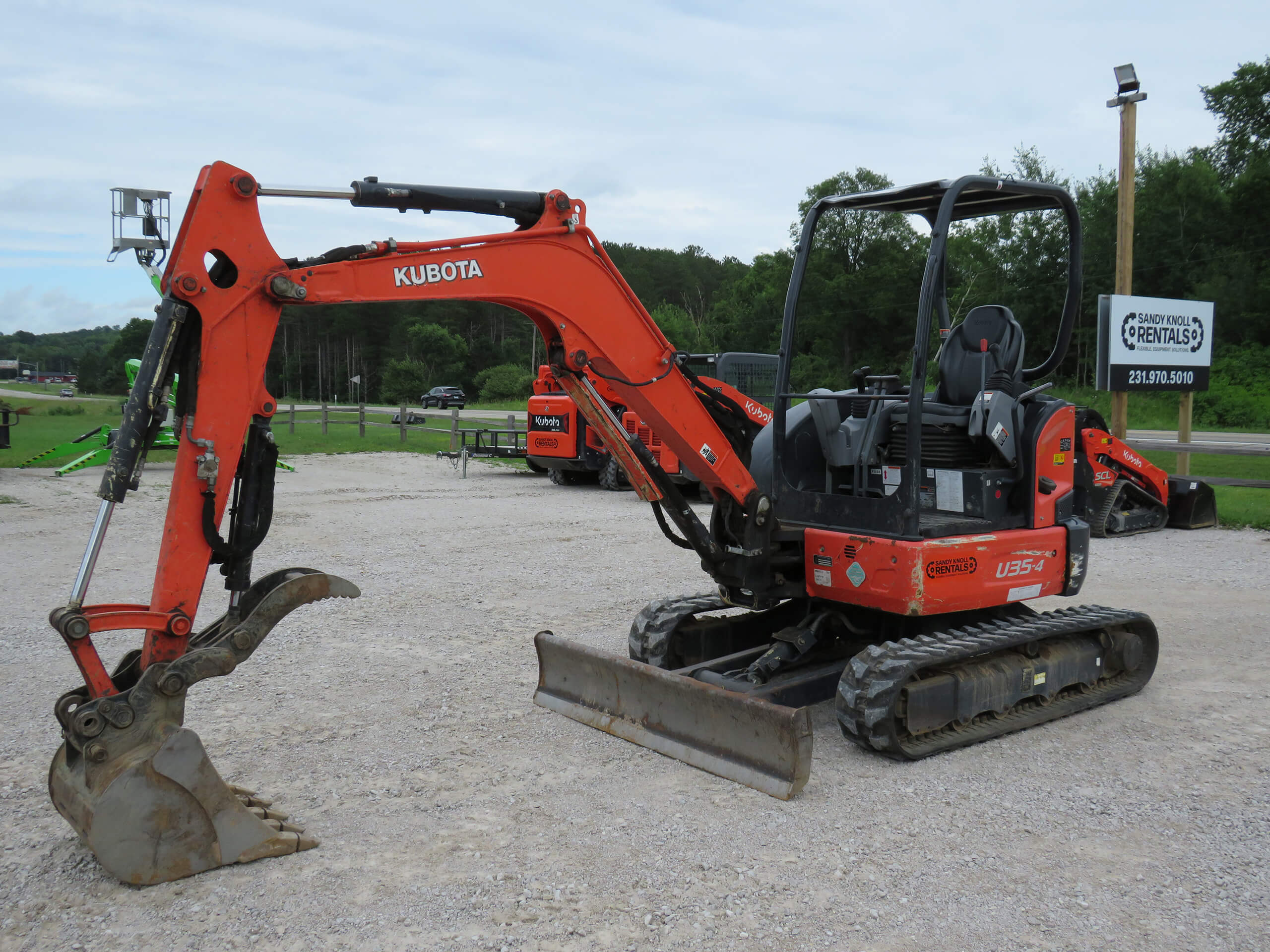 An orange Kubota U35-4 mini excavator with a bucket attachment is parked on a gravel lot near a rental facility.