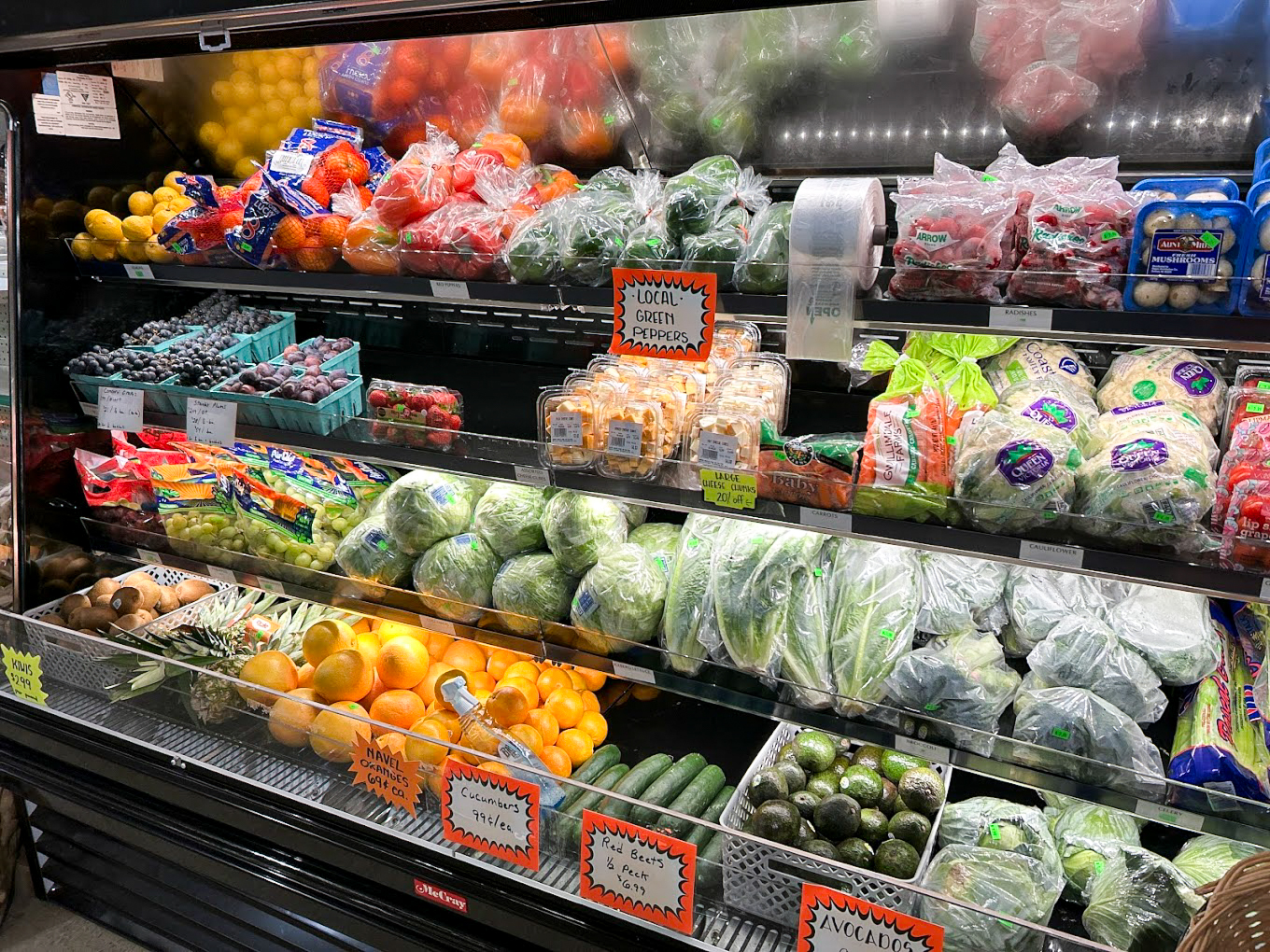 Country Variety Store Bellafontaine OH A grocery store produce display with various fruits and vegetables, including lettuce, avocados, oranges, grapes, berries, tomatoes, and packaged leafy greens.