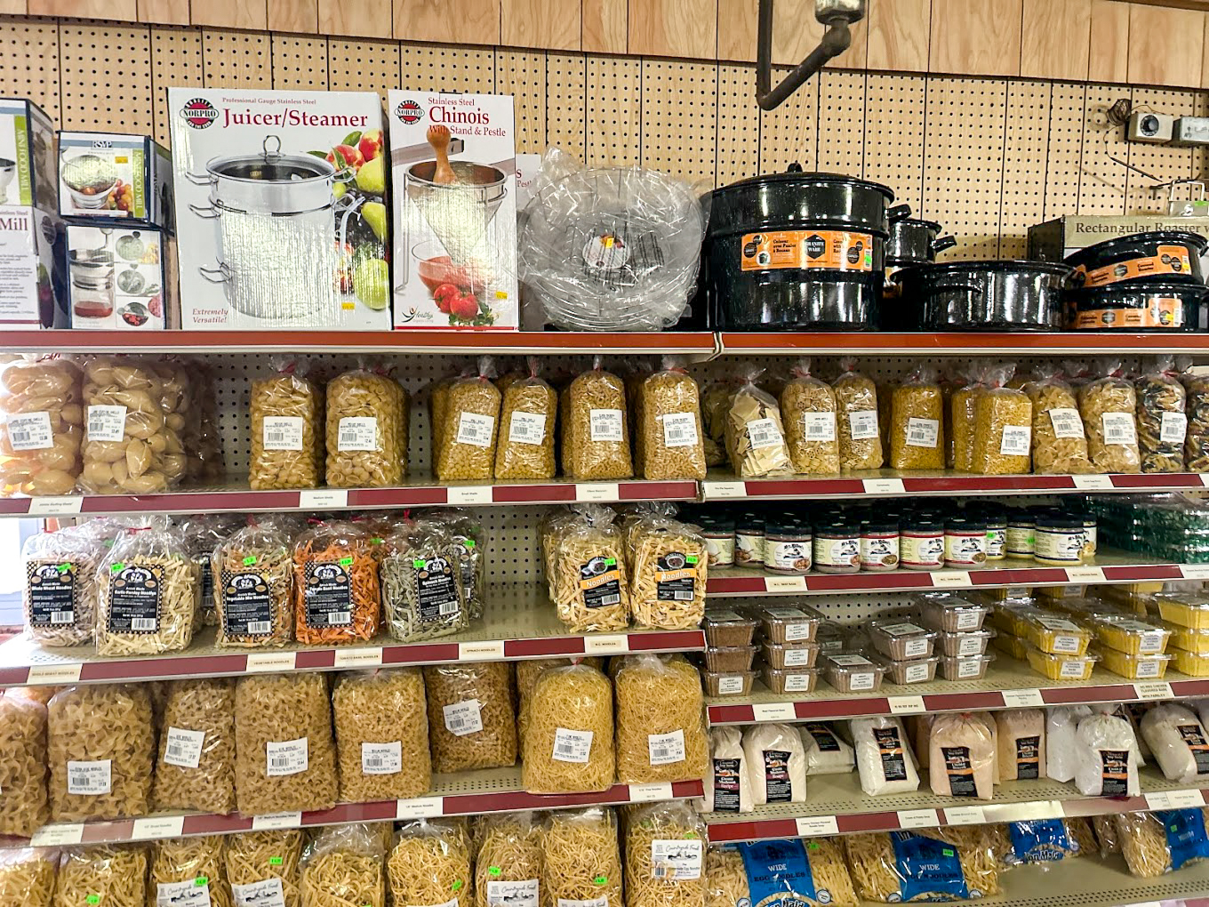 Country Variety Store Bellafontaine OH Shelves stocked with various dry pasta, packaged baked goods, cooking pots, plastic bowls, and kitchen equipment in a grocery store.