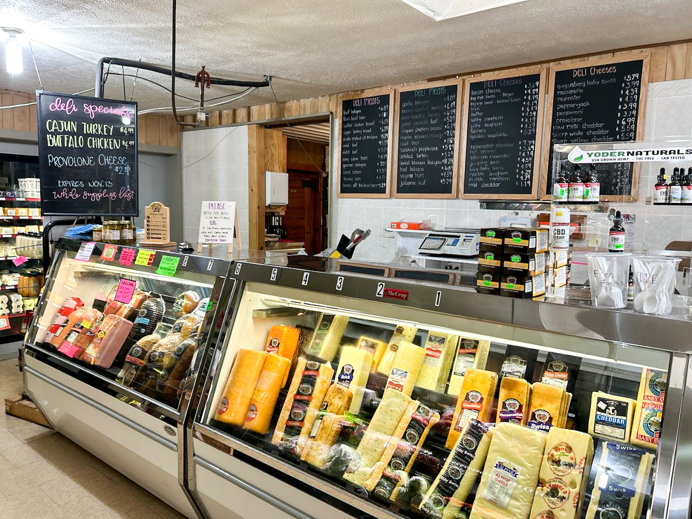Country Variety Store Bellafontaine OH A deli counter displays a variety of cheeses, with menu boards and deli specials listed on chalkboards in the background.