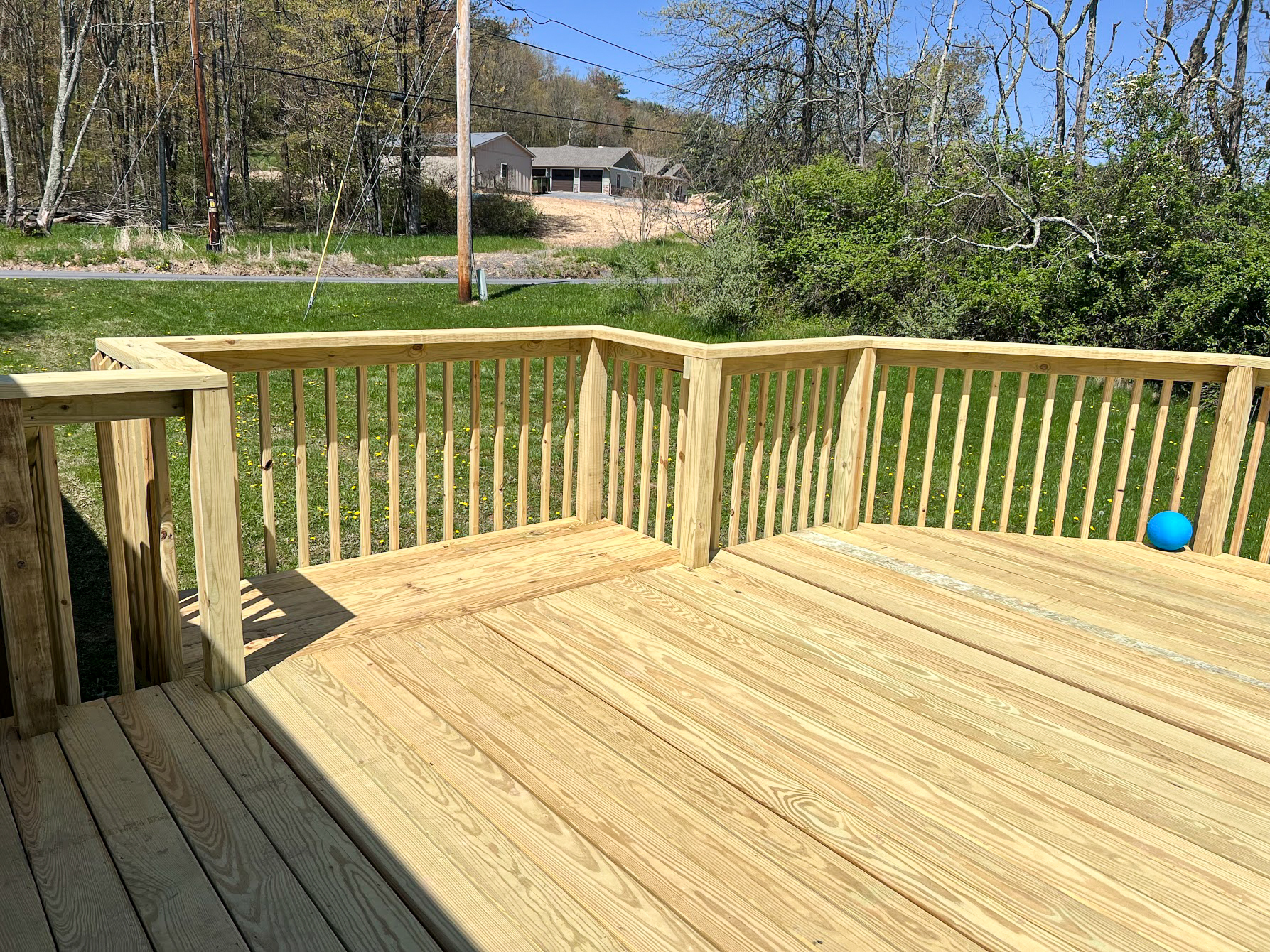 HMG Construction Mill Hall, PA A newly constructed wooden deck with a railing overlooks a grassy backyard; a blue ball is on the lawn near the deck.