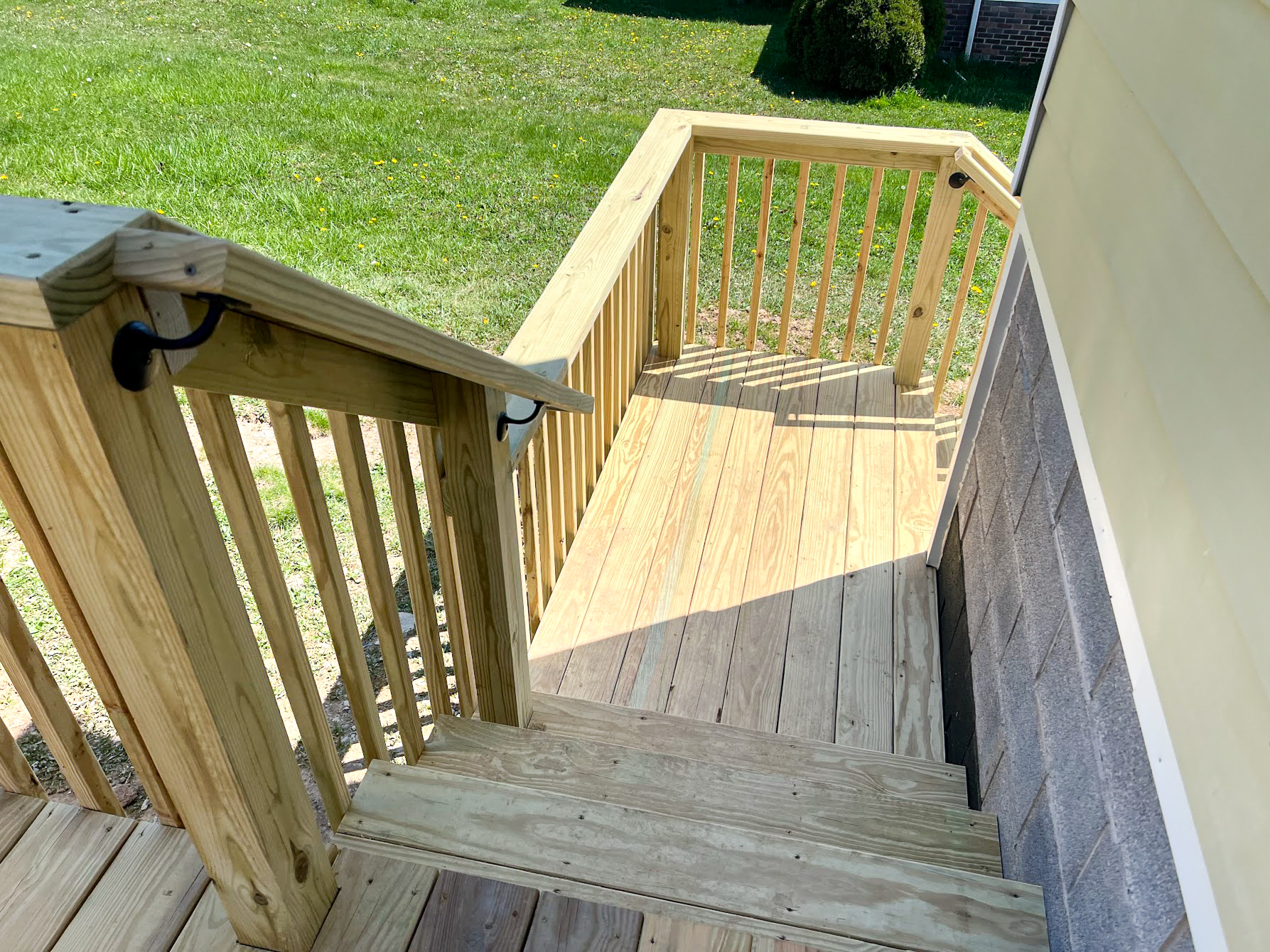 HMG Construction Mill Hall, PA Wooden steps and railing lead down from a porch to a grass yard, adjacent to a house with a concrete foundation.
