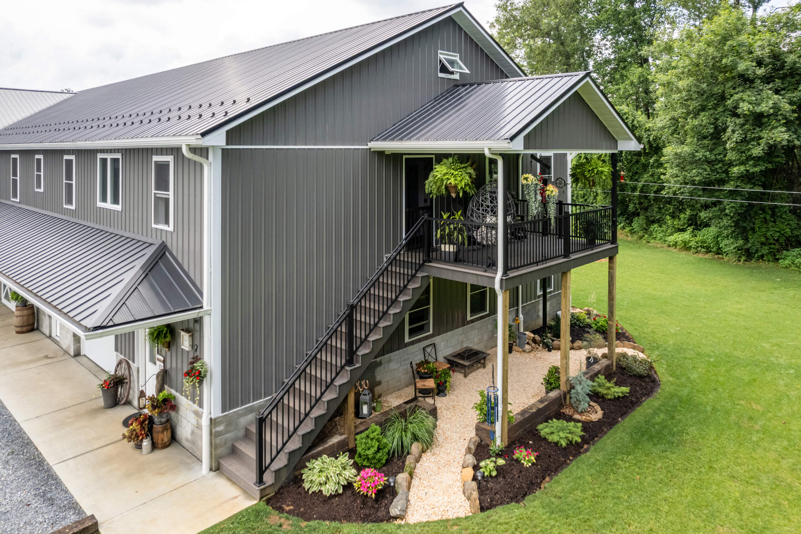 Pine Tree Builders Honeybrook Chester Lancaster County PA Modern two-story gray metal barn-style house with exterior staircase, covered balcony, landscaped garden, and neatly maintained lawn.