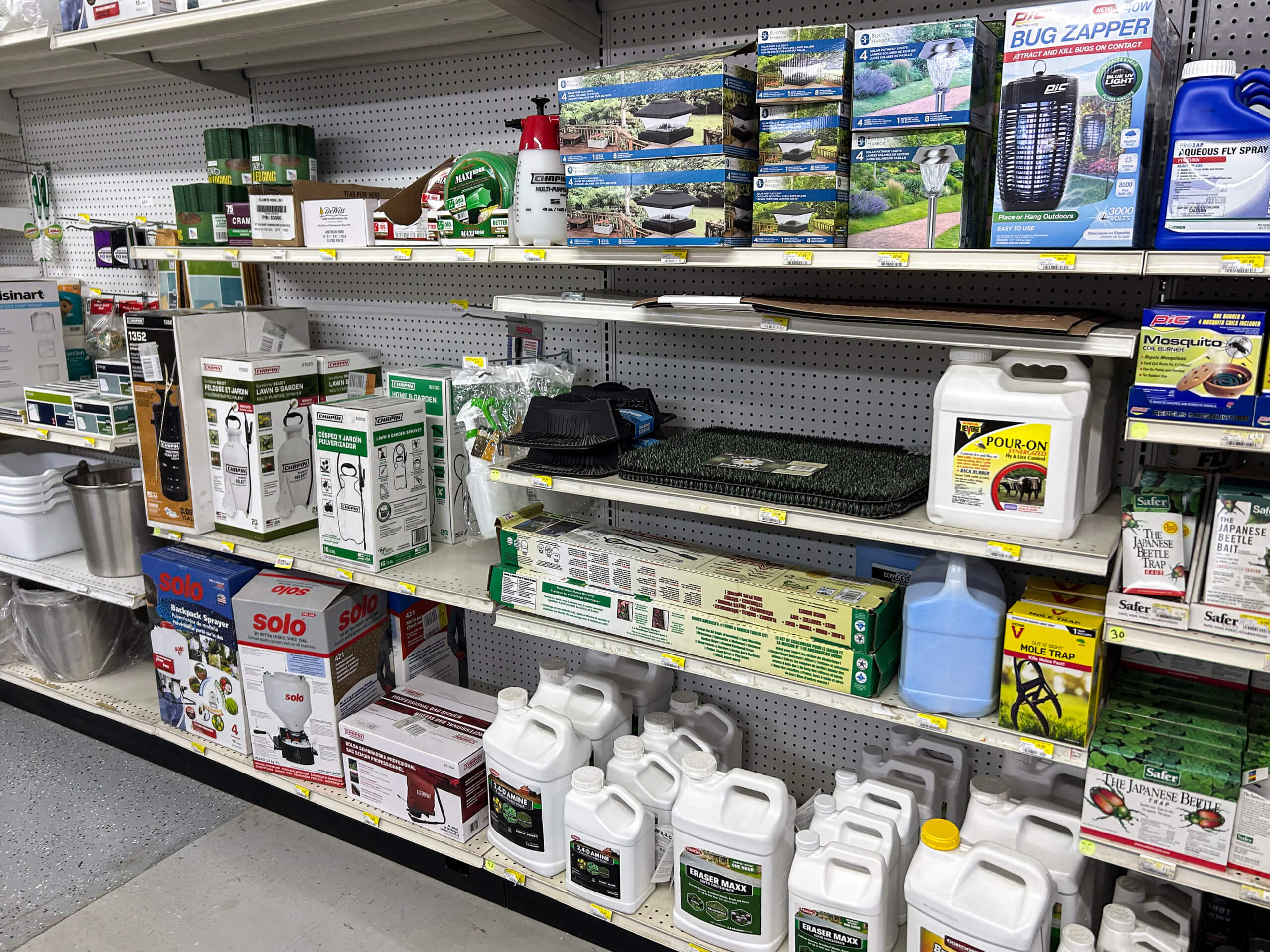 Benny's Hardware Barnett MO Store shelf stocked with bug zappers, mosquito repellents, pond kits, plant food, and gardening supplies, organized in rows on white metal shelves.