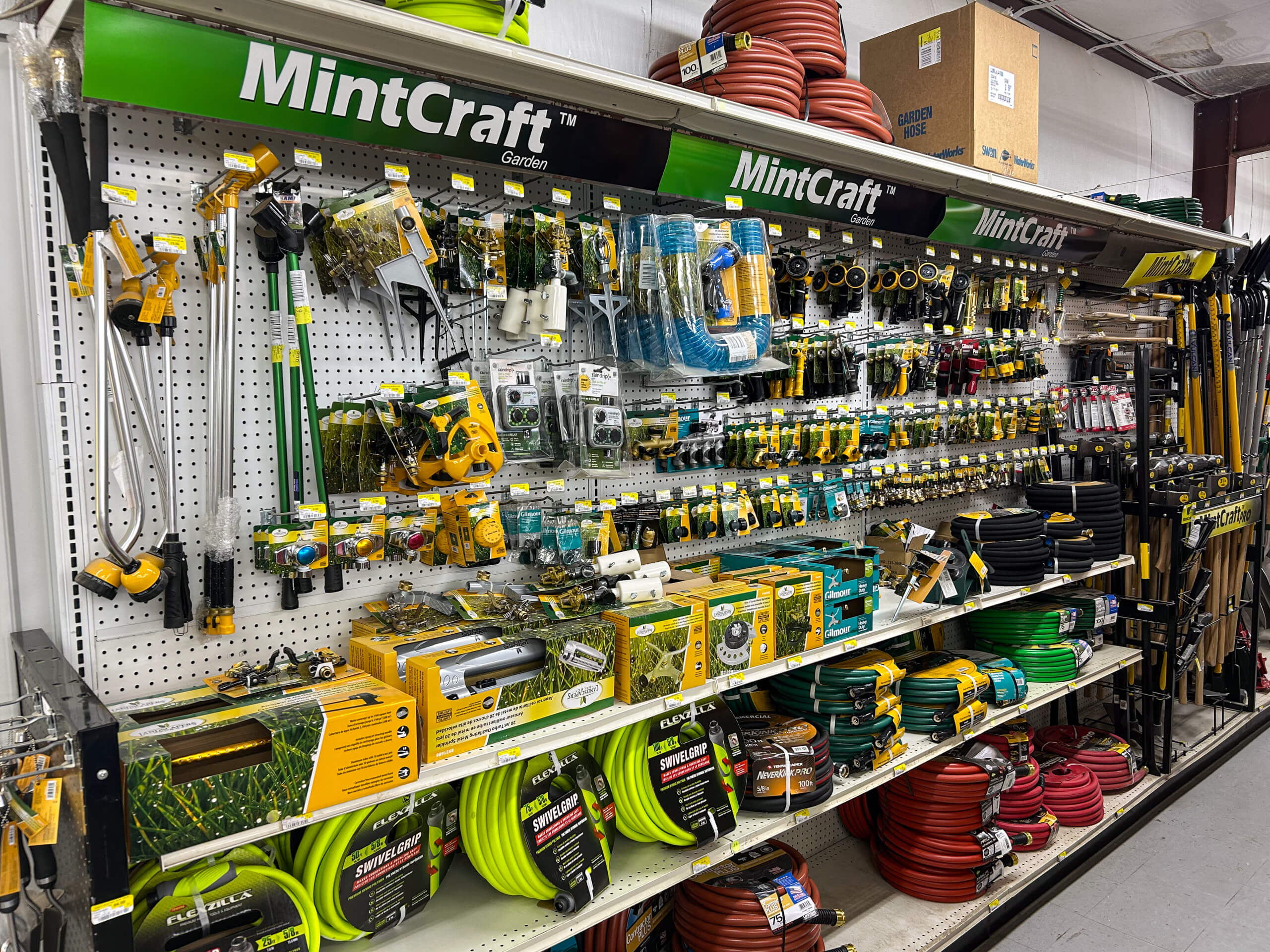 Benny's Hardware Barnett MO A store shelf displays assorted MintCraft garden tools, hoses, hose nozzles, and watering accessories organized in rows.