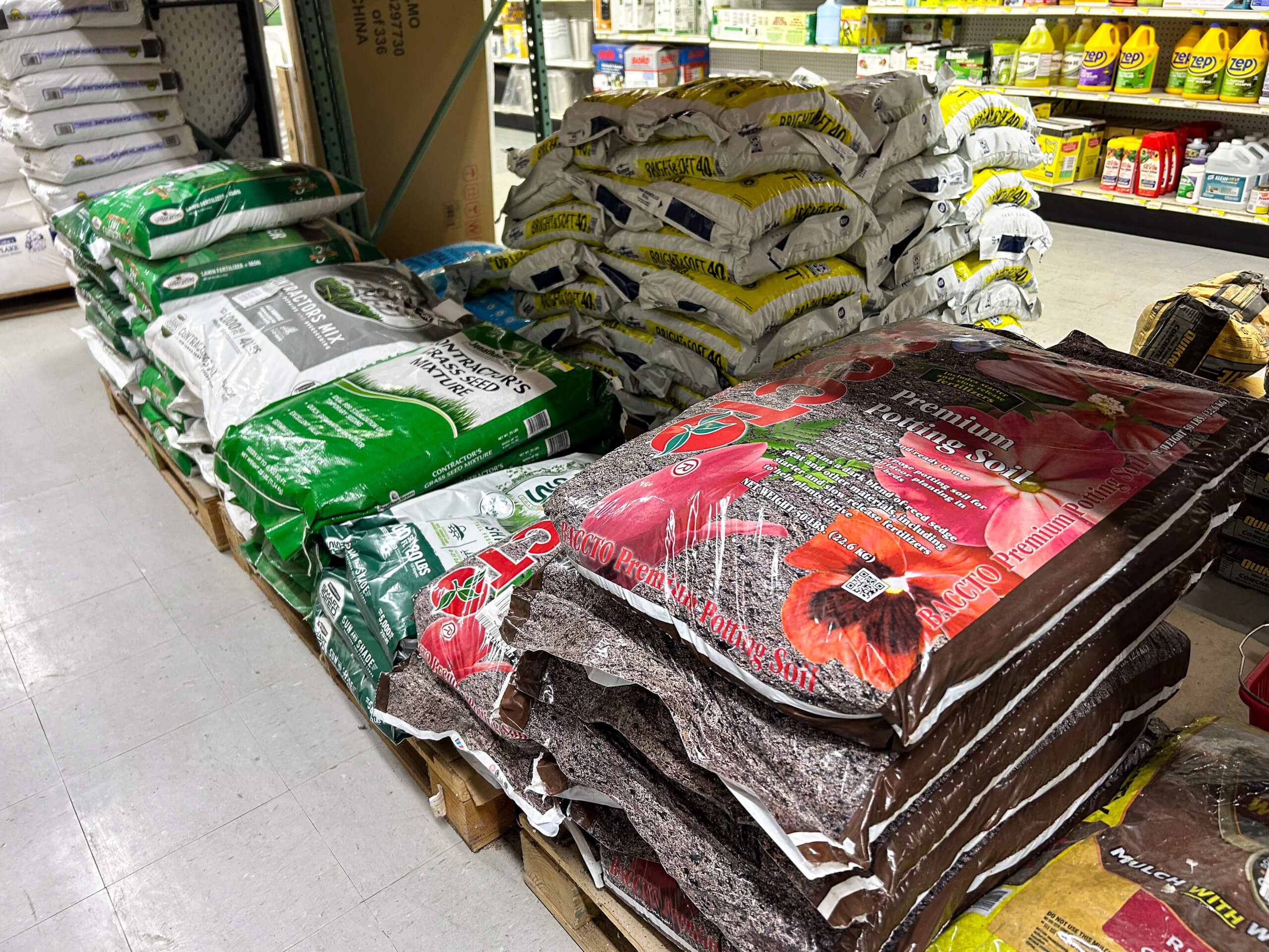 Benny's Hardware Barnett MO Bags of gardening soil and mulch stacked on pallets inside a store, with shelves of lawn and garden products visible in the background.
