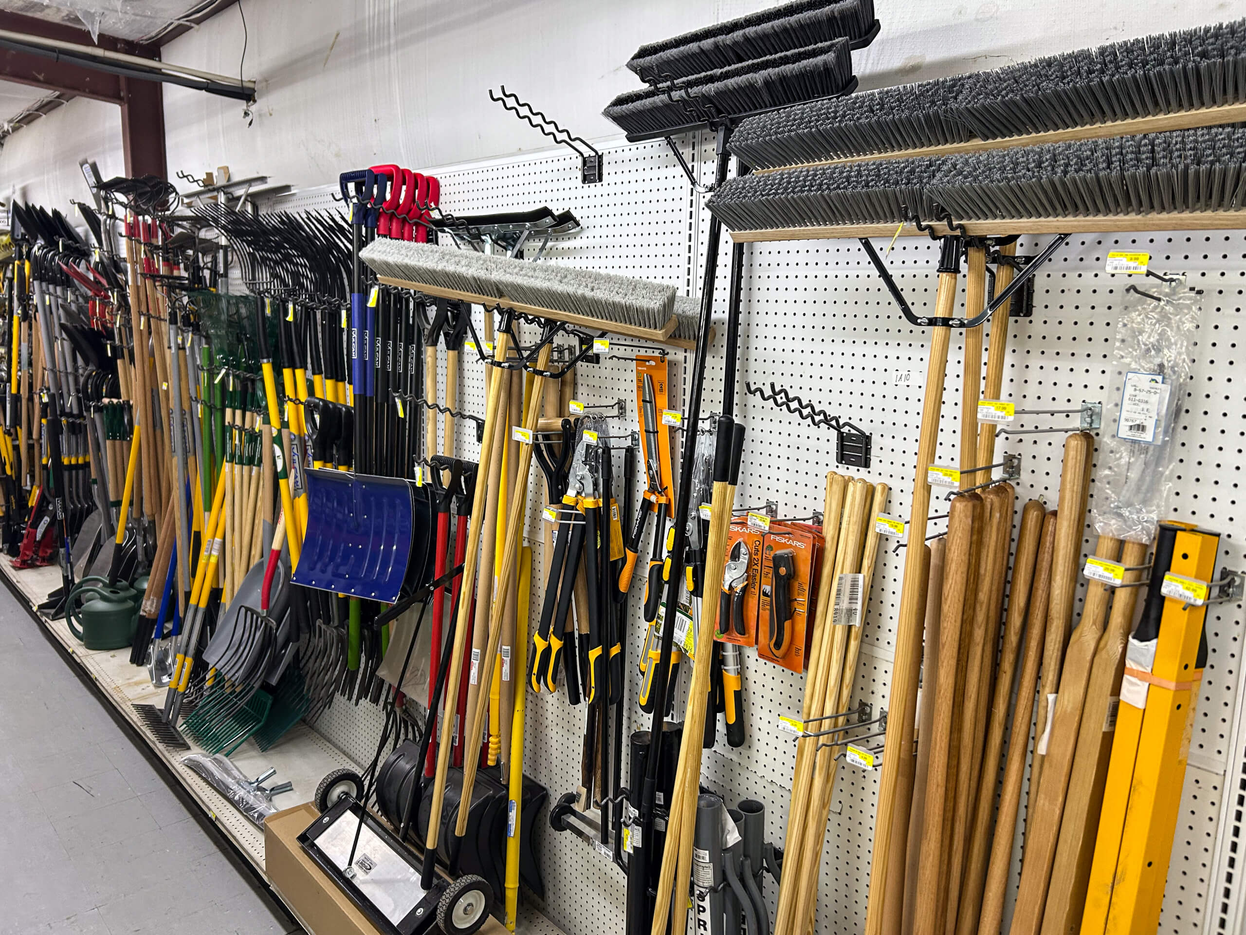 Benny's Hardware Barnett MO A store aisle display with various gardening and landscaping tools, including rakes, shovels, brooms, and hoes, hanging on a pegboard wall.