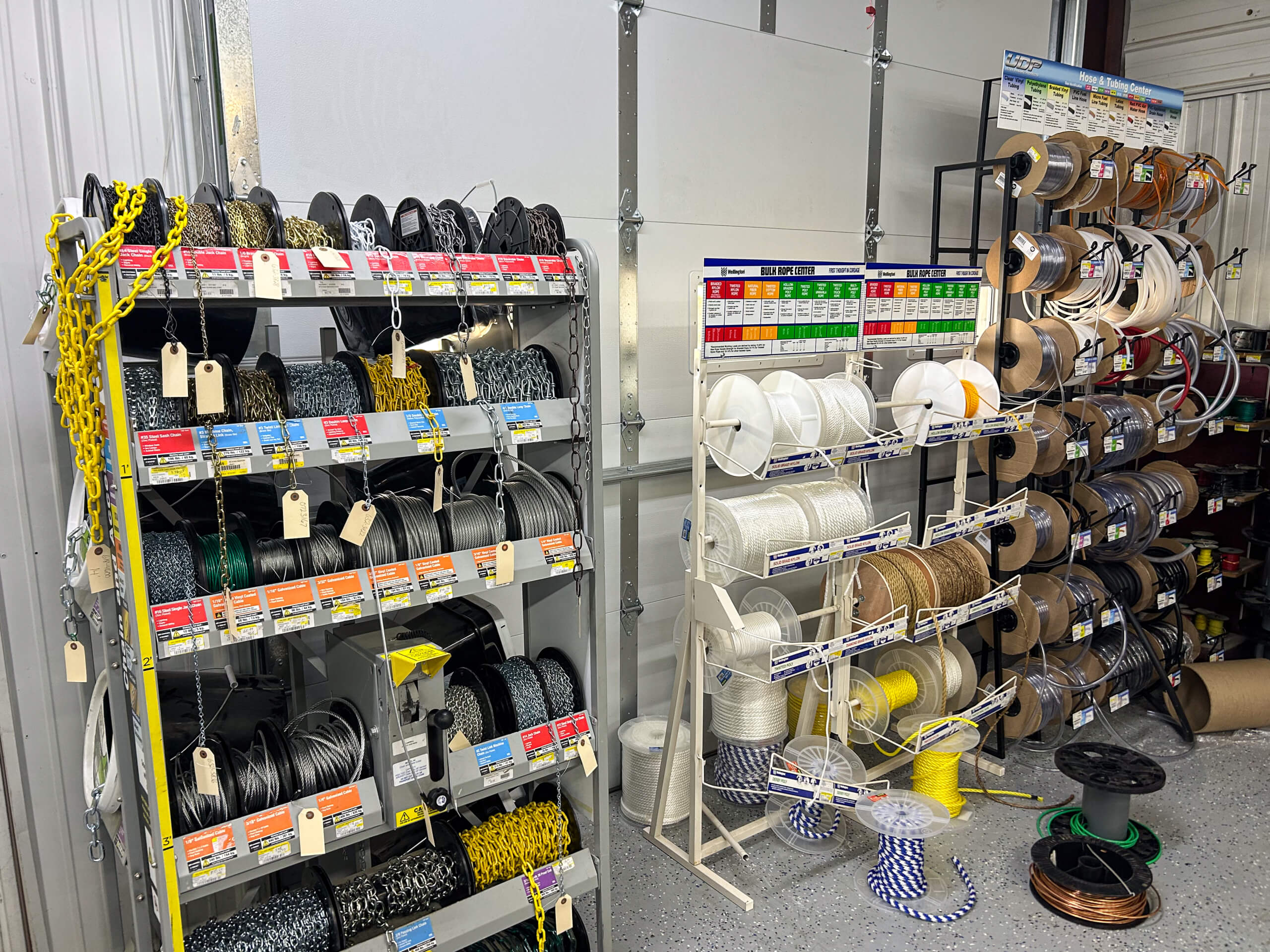 Benny's Hardware Barnett MO Shelves holding various spools of chains, ropes, and cables are organized by type and color in a hardware store setting.