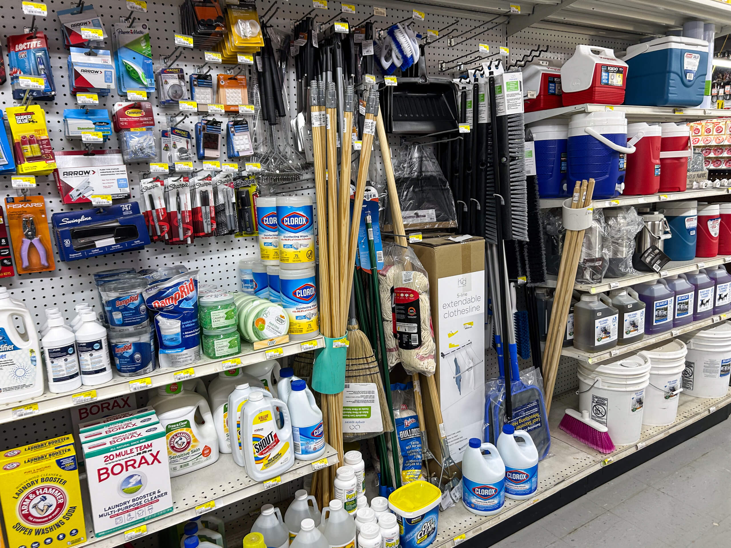 Benny's Hardware Barnett MO Store aisle shelf stocked with cleaning supplies, bleach, buckets, coolers, scrubbing brushes, and other household products.