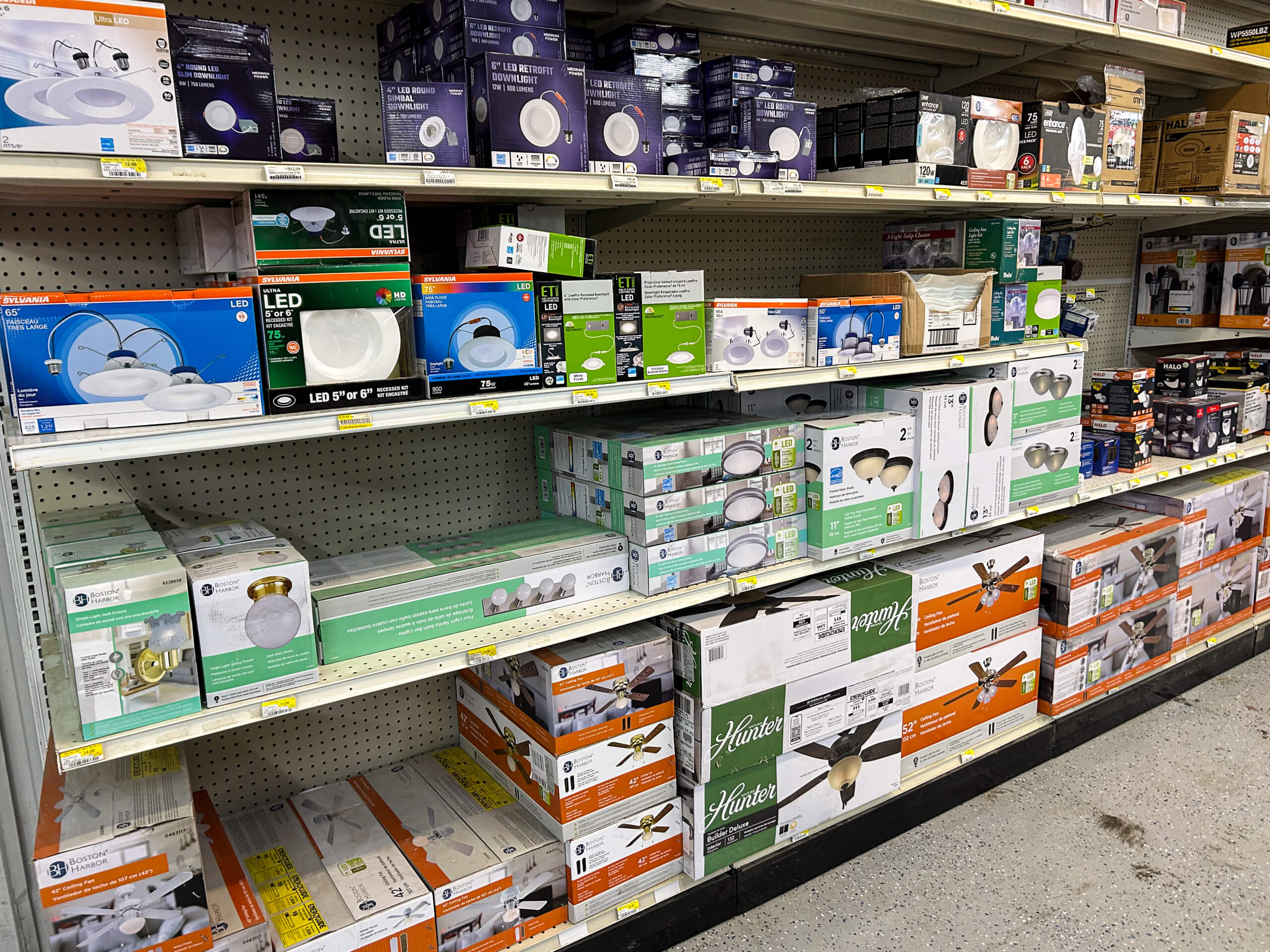 Benny's Hardware Barnett MO Shelves stocked with various ceiling lights, light fixtures, and fan kits in a hardware or home improvement store aisle.