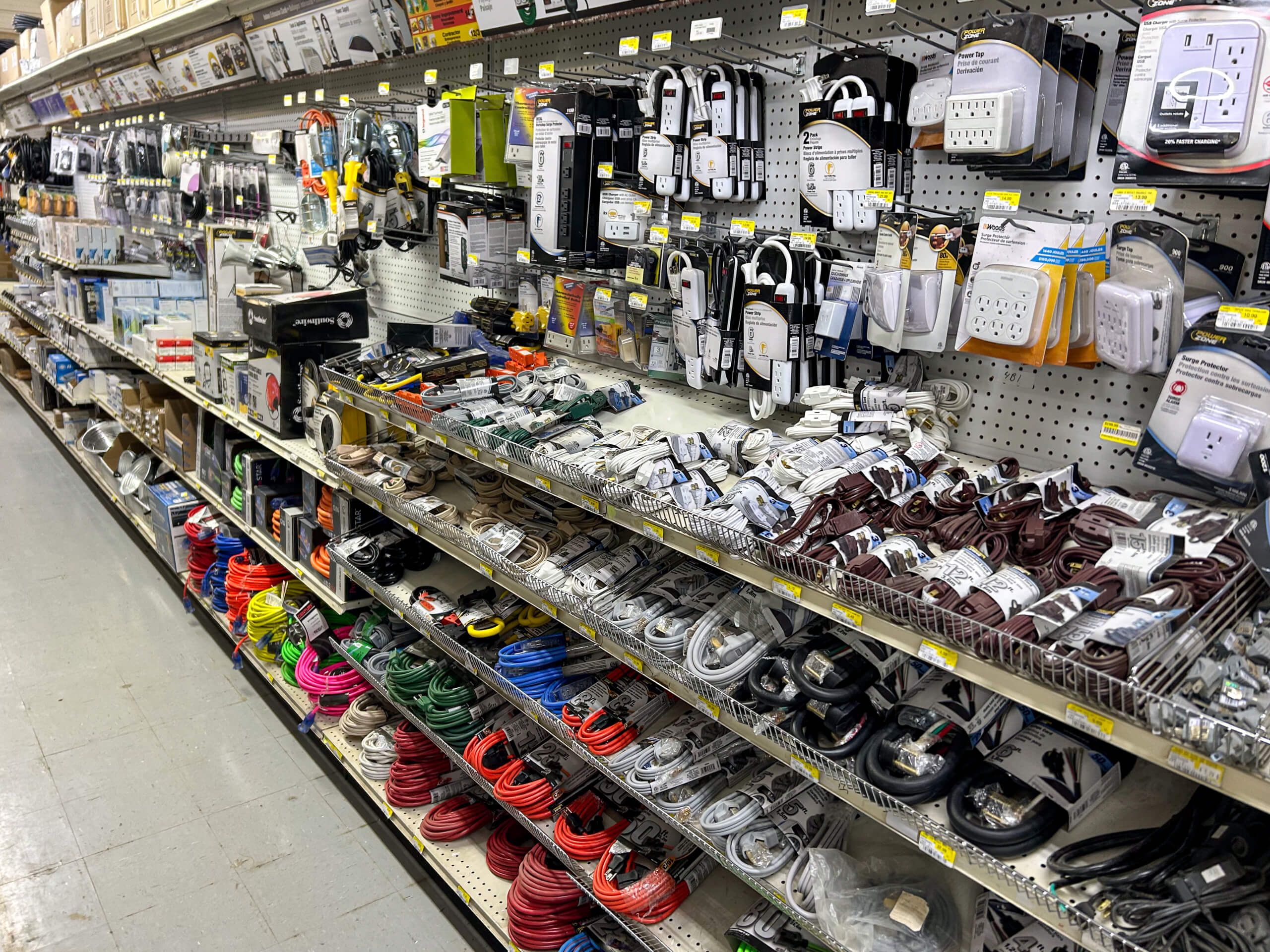 Benny's Hardware Barnett MO Shelves in a hardware store aisle display a variety of electrical supplies, including cords, power strips, outlets, and extension cables organized by type and color.