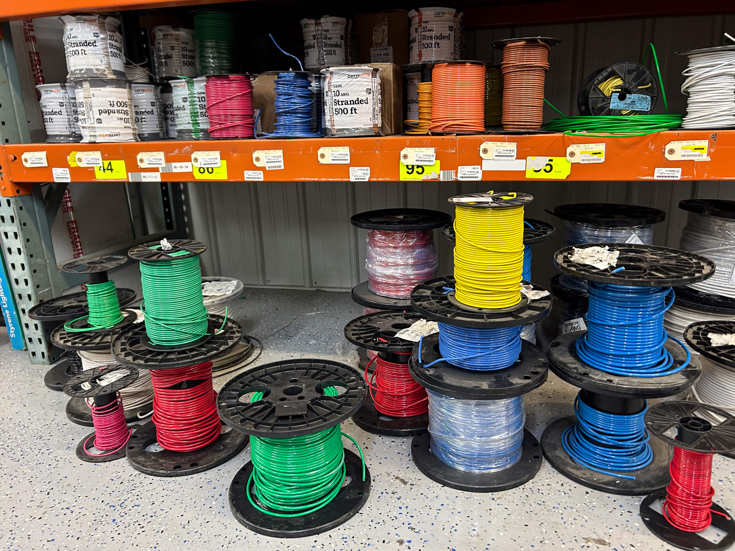 Benny's Hardware Barnett MO Spools of colored electrical wire are stacked on the floor and shelves in a hardware store aisle. Labels with prices are visible on the orange shelf.