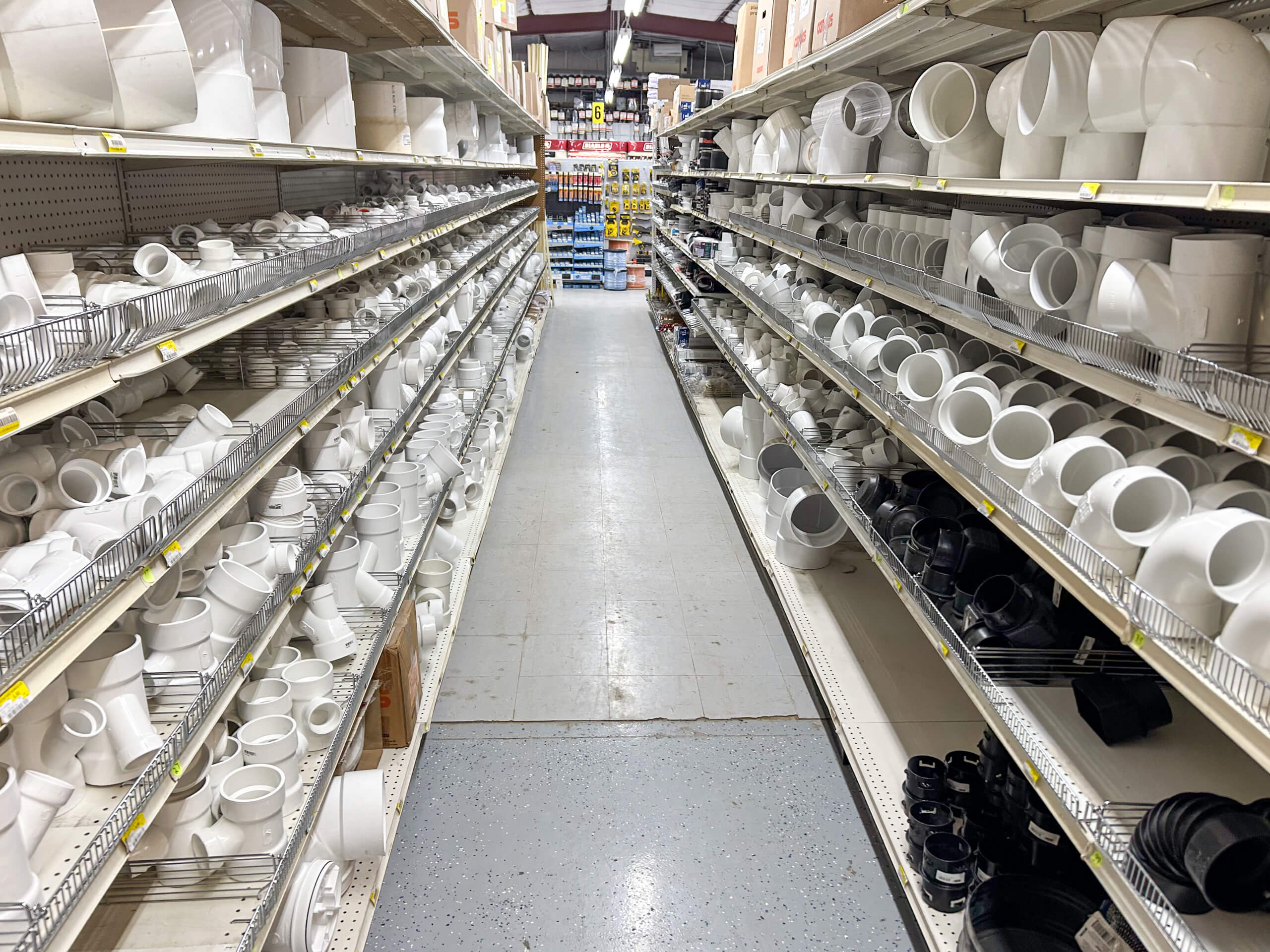 Benny's Hardware Barnett MO A store aisle lined with shelves filled with various white and black plastic plumbing pipe fittings and connectors.