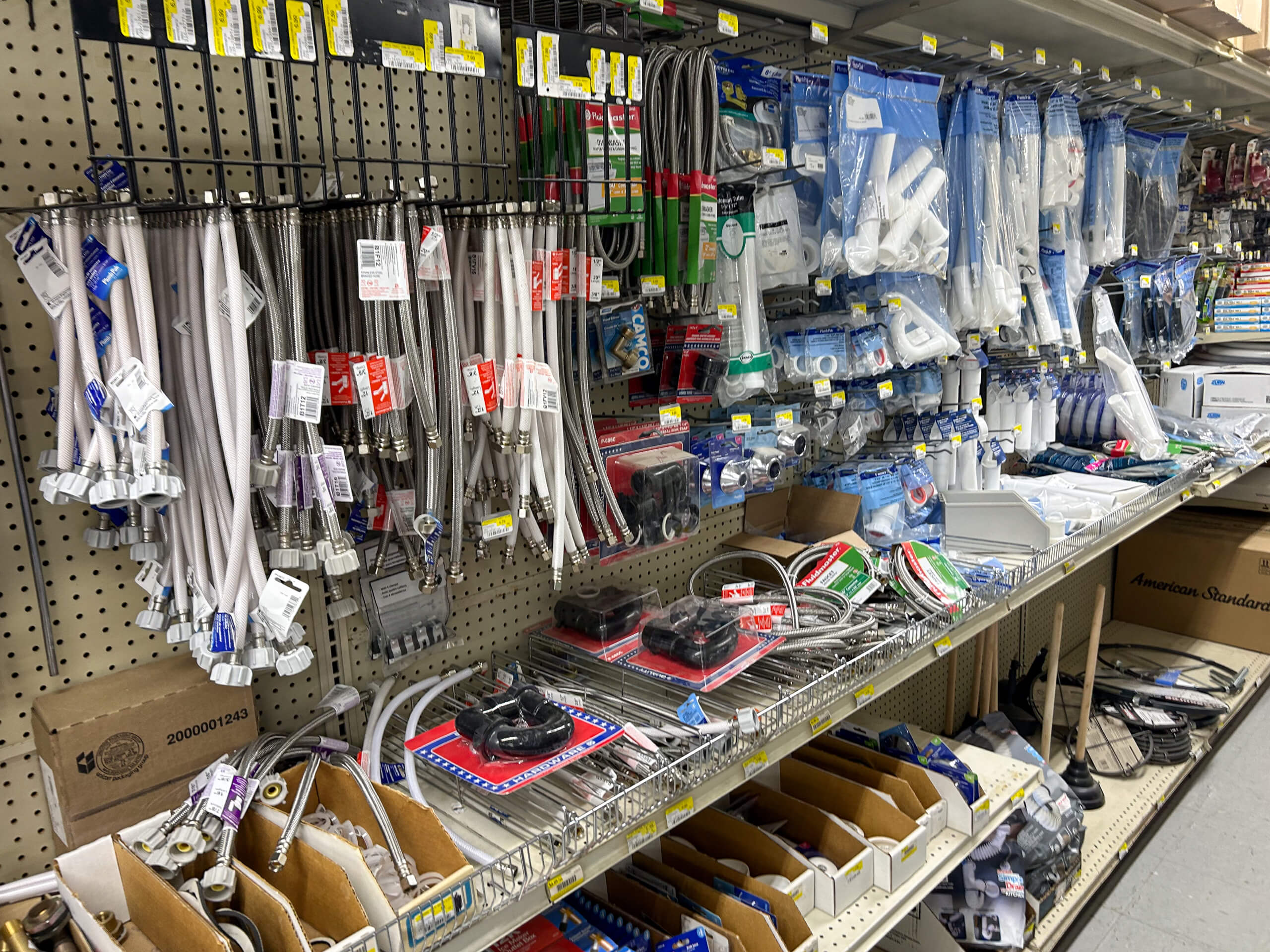 Benny's Hardware Barnett MO A store aisle with shelves displaying various plumbing supplies, including hoses, pipes, fittings, and packaged tools hanging on hooks and arranged in bins.