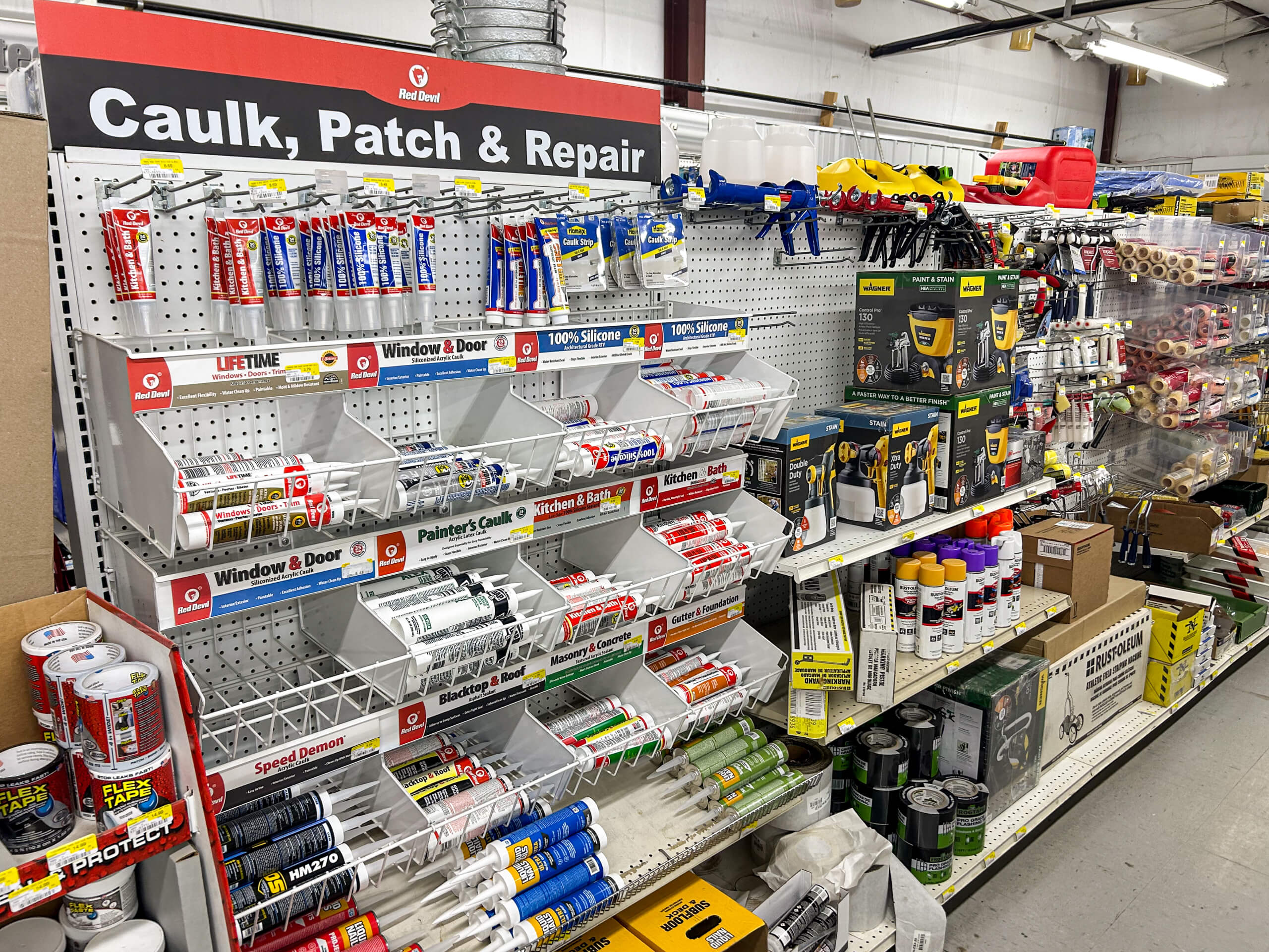 Benny's Hardware Barnett MO A hardware store aisle displays caulks, sealants, patching products, and tools on shelves and pegboards under a sign reading "Caulk, Patch & Repair.