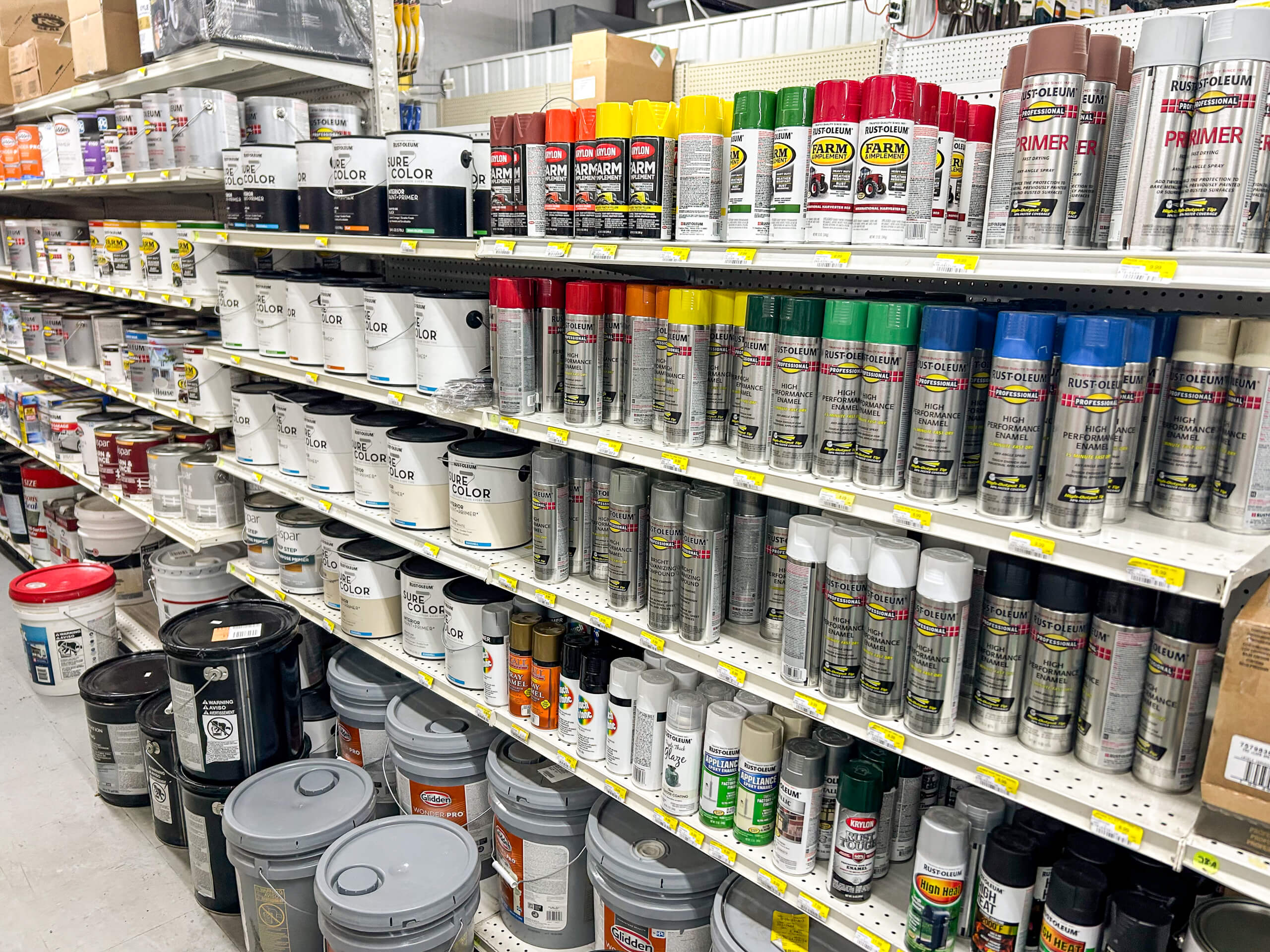 Benny's Hardware Barnett MO Shelves in a store stocked with various cans of spray paint, paint buckets, and painting supplies arranged by color and type.