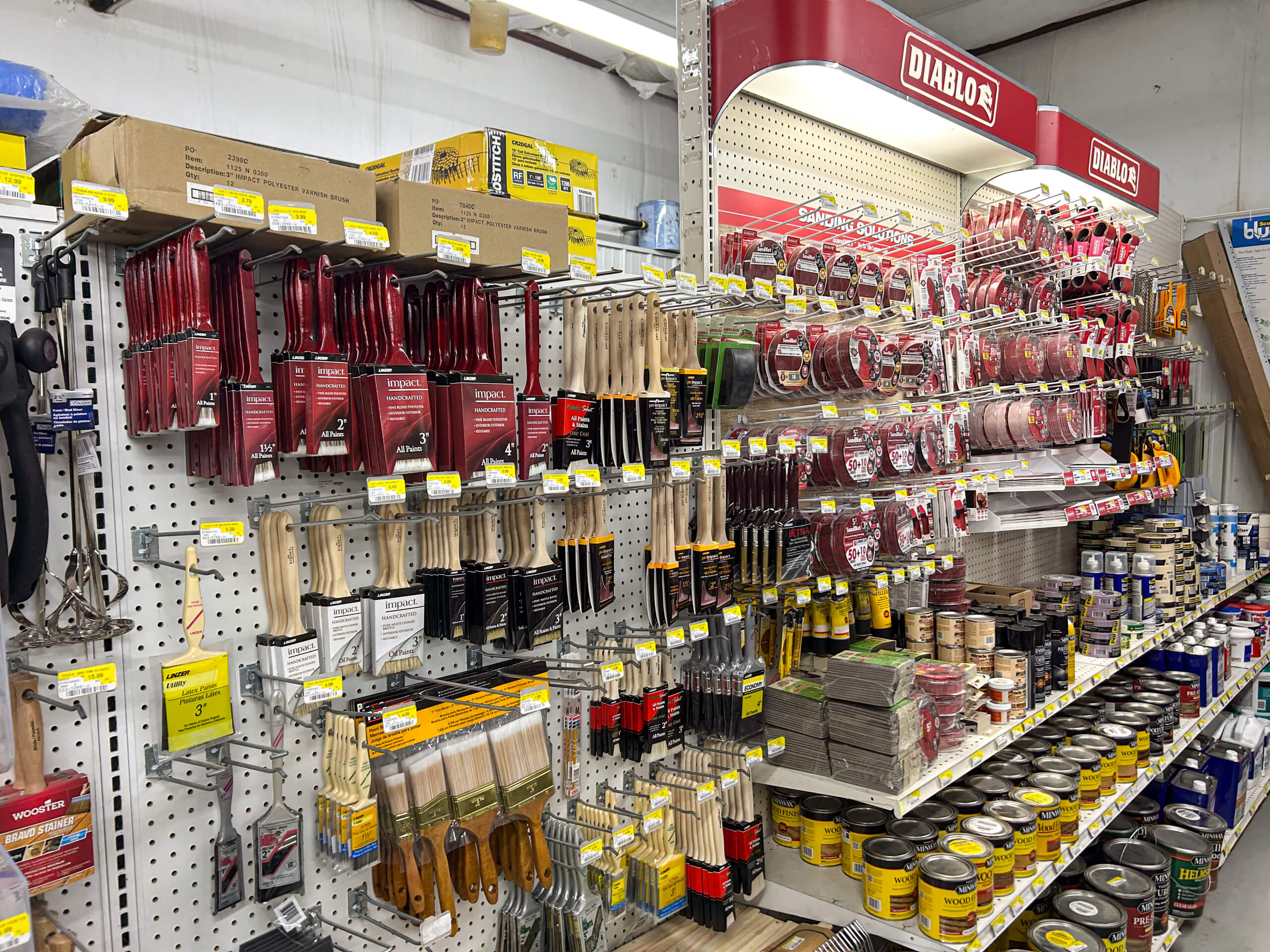 Benny's Hardware Barnett MO Store aisle shelf displaying various paintbrushes, sanding discs, and painting supplies, with clearly marked yellow price tags.