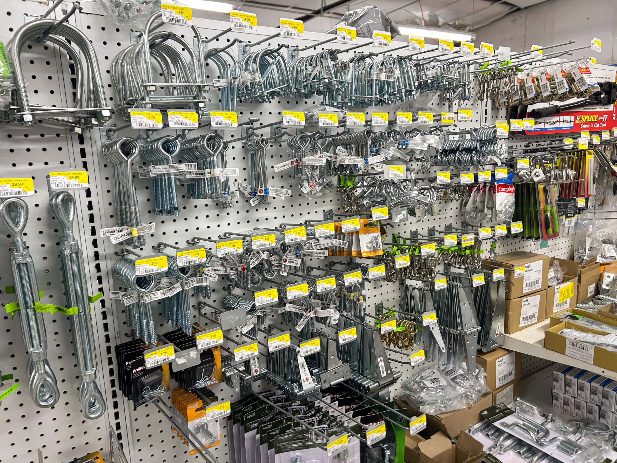 Benny's Hardware Barnett MO A hardware store display of metal fasteners, brackets, hooks, and other hardware items hanging on a pegboard wall, each labeled with yellow price tags.