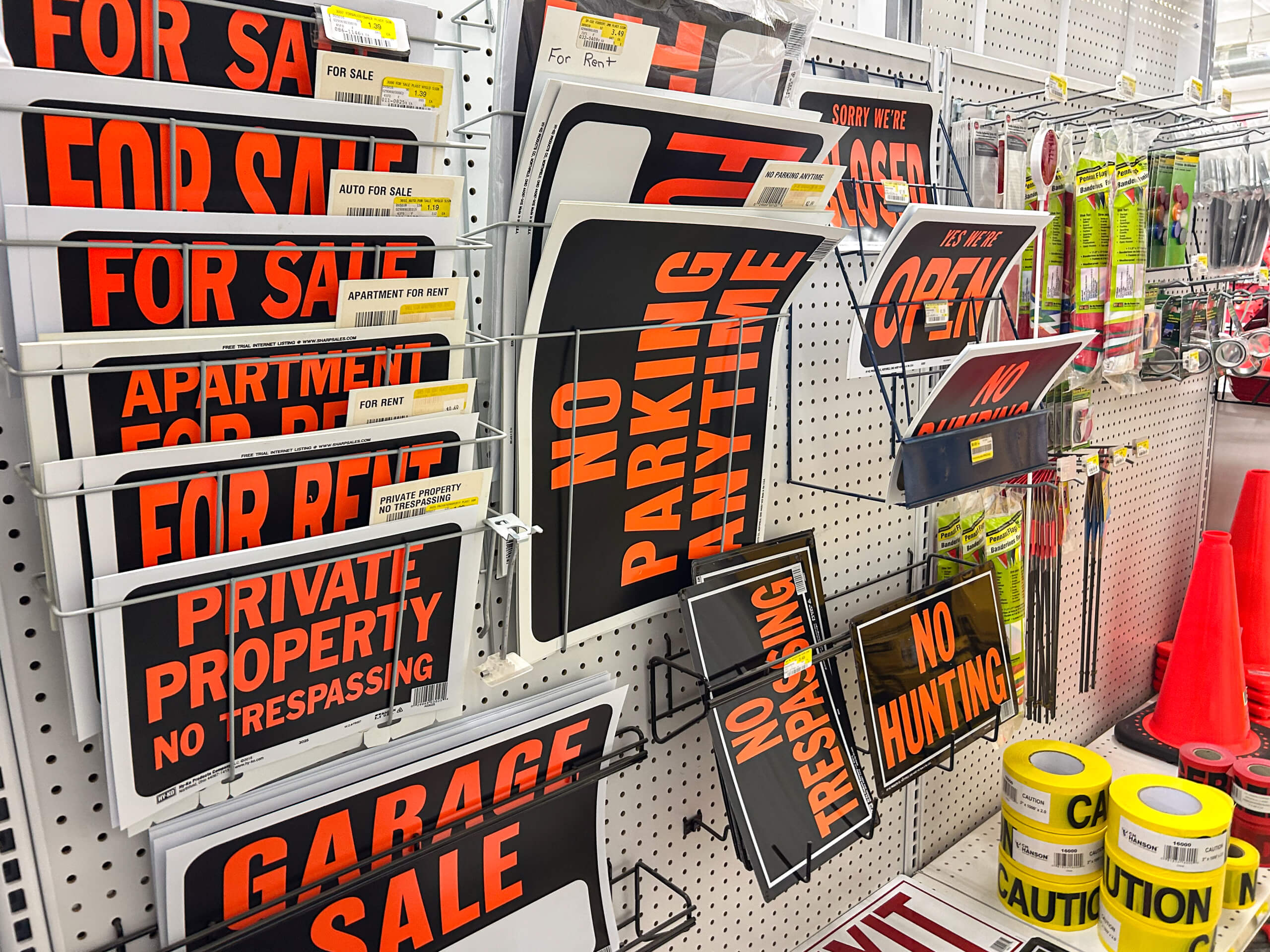 Benny's Hardware Barnett MO A store display with various signs including “For Sale,” “For Rent,” “No Parking Anytime,” “No Trespassing,” “No Hunting,” and rolls of caution tape on a pegboard wall.