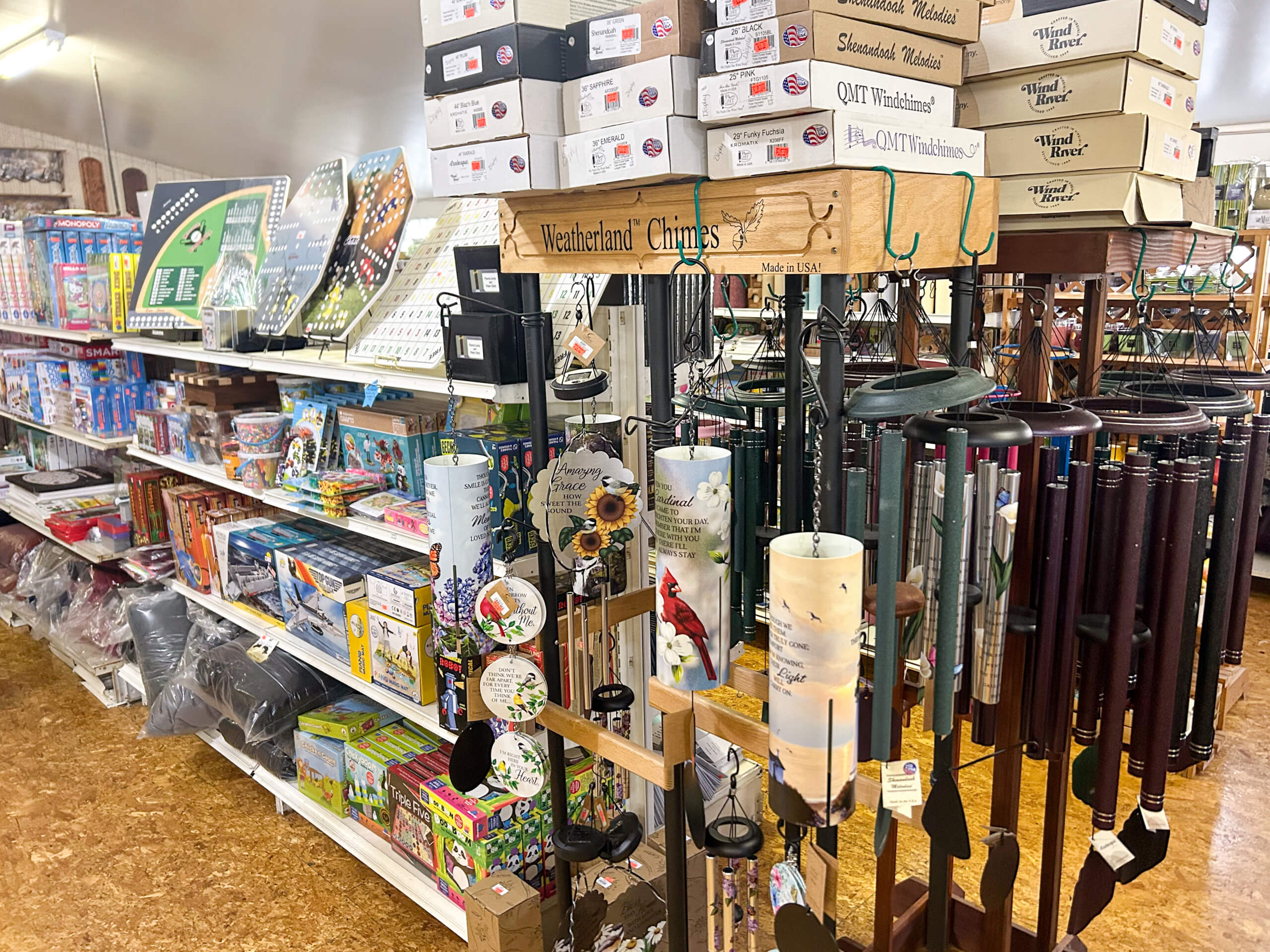 Miller's Country Store Grabill IN A store aisle displays wind chimes, bird feeders, board games, puzzles, and various boxed items stacked on shelves.