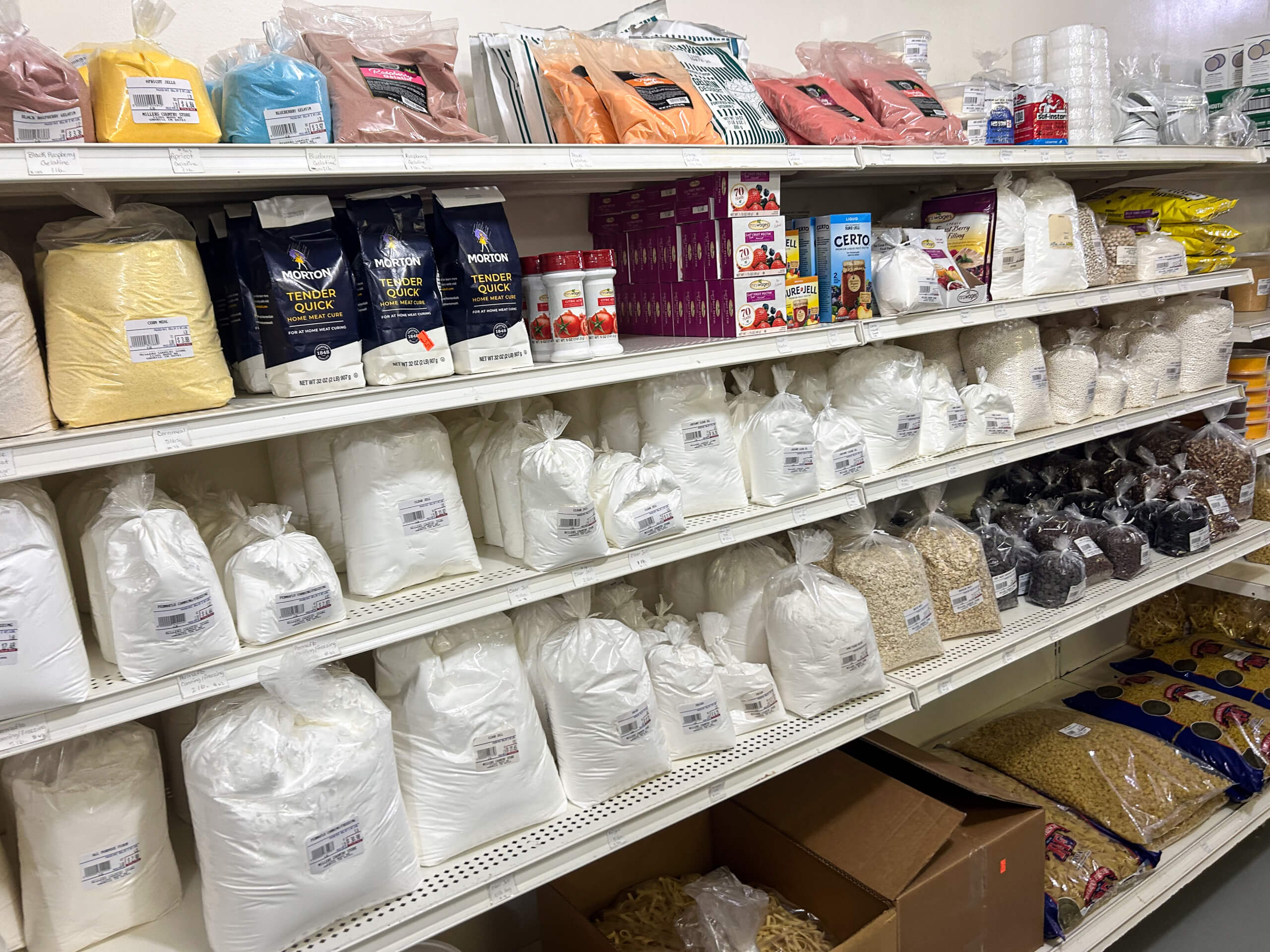 Miller's Country Store Grabill IN Shelves in a grocery store lined with various packaged dry goods, including flour, grains, pasta, baking mixes, and cereals in plastic and paper bags.