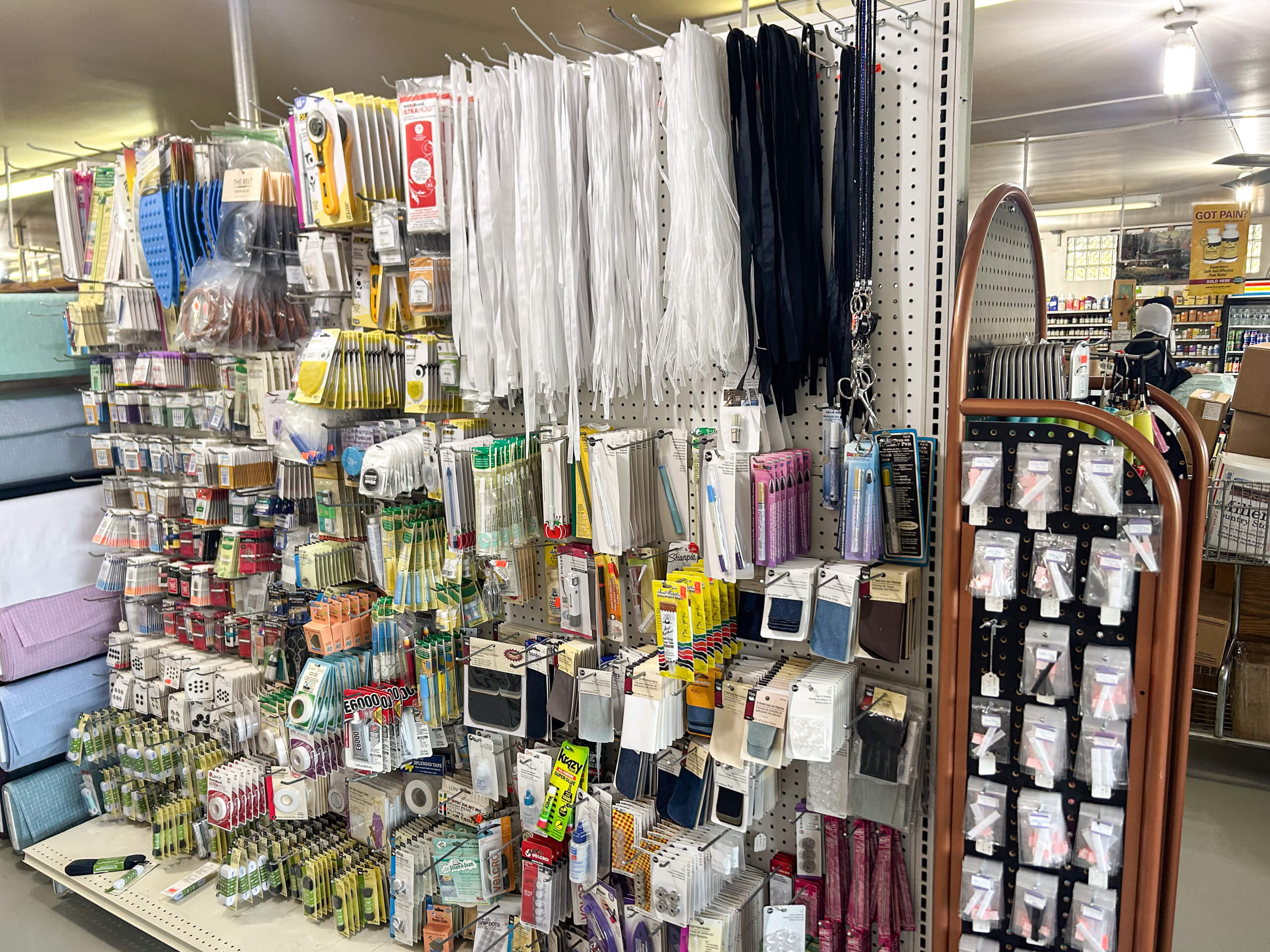 Miller's Country Store Grabill IN Display of assorted sewing and craft supplies on shelves, including zippers, elastics, needles, thread, measuring tapes, and other notions in a well-lit store aisle.