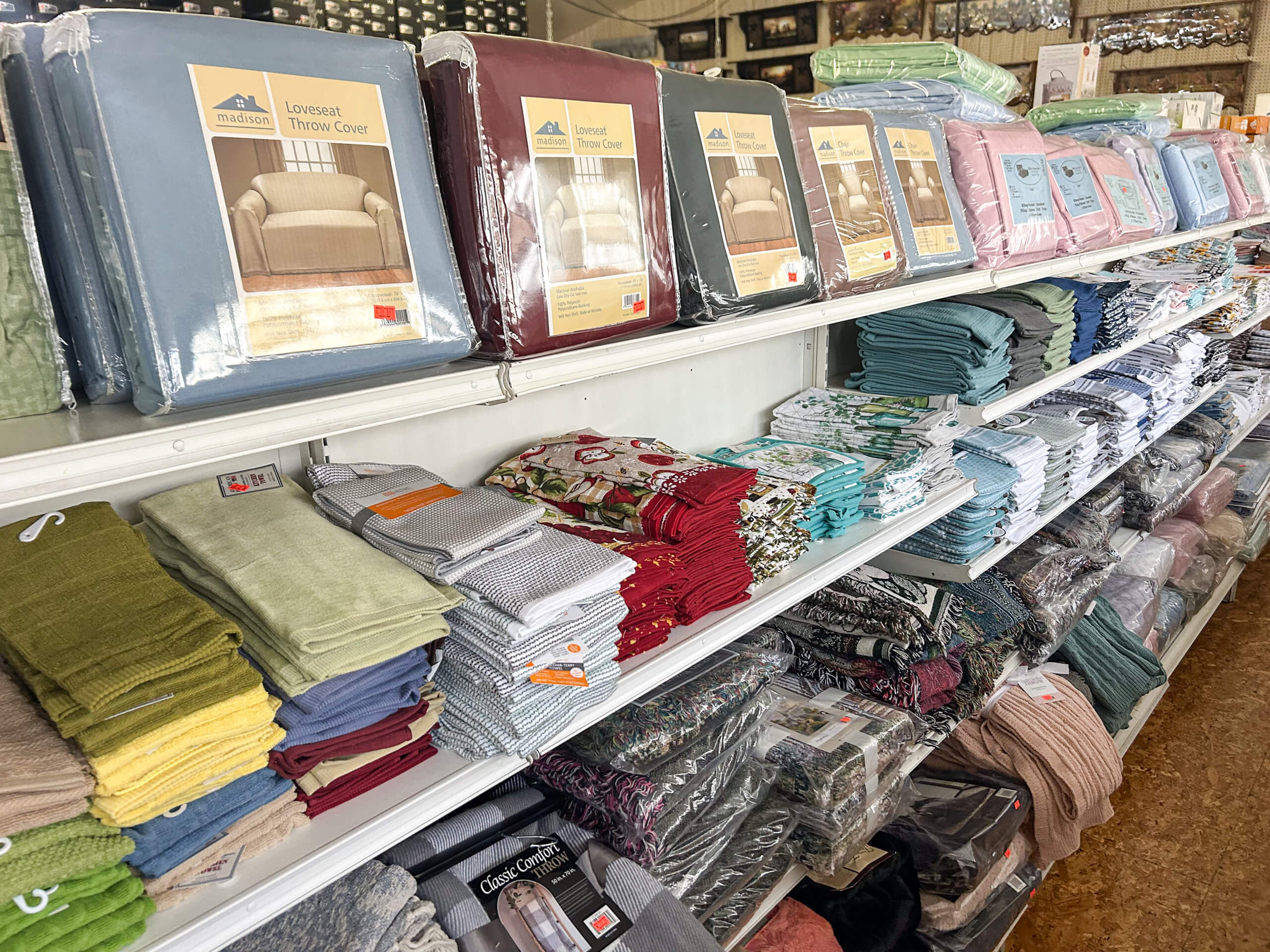 Miller's Country Store Grabill IN Shelves stocked with various folded bed linens, throw covers, towels, and bedding sets in different colors and packaging.