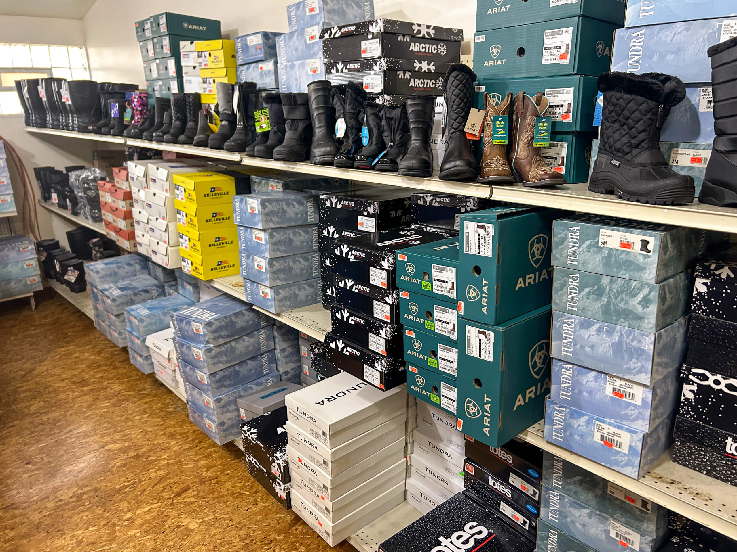Miller's Country Store Grabill IN Shelves stocked with various brands of winter boots, including boxed pairs and display models in a store setting.