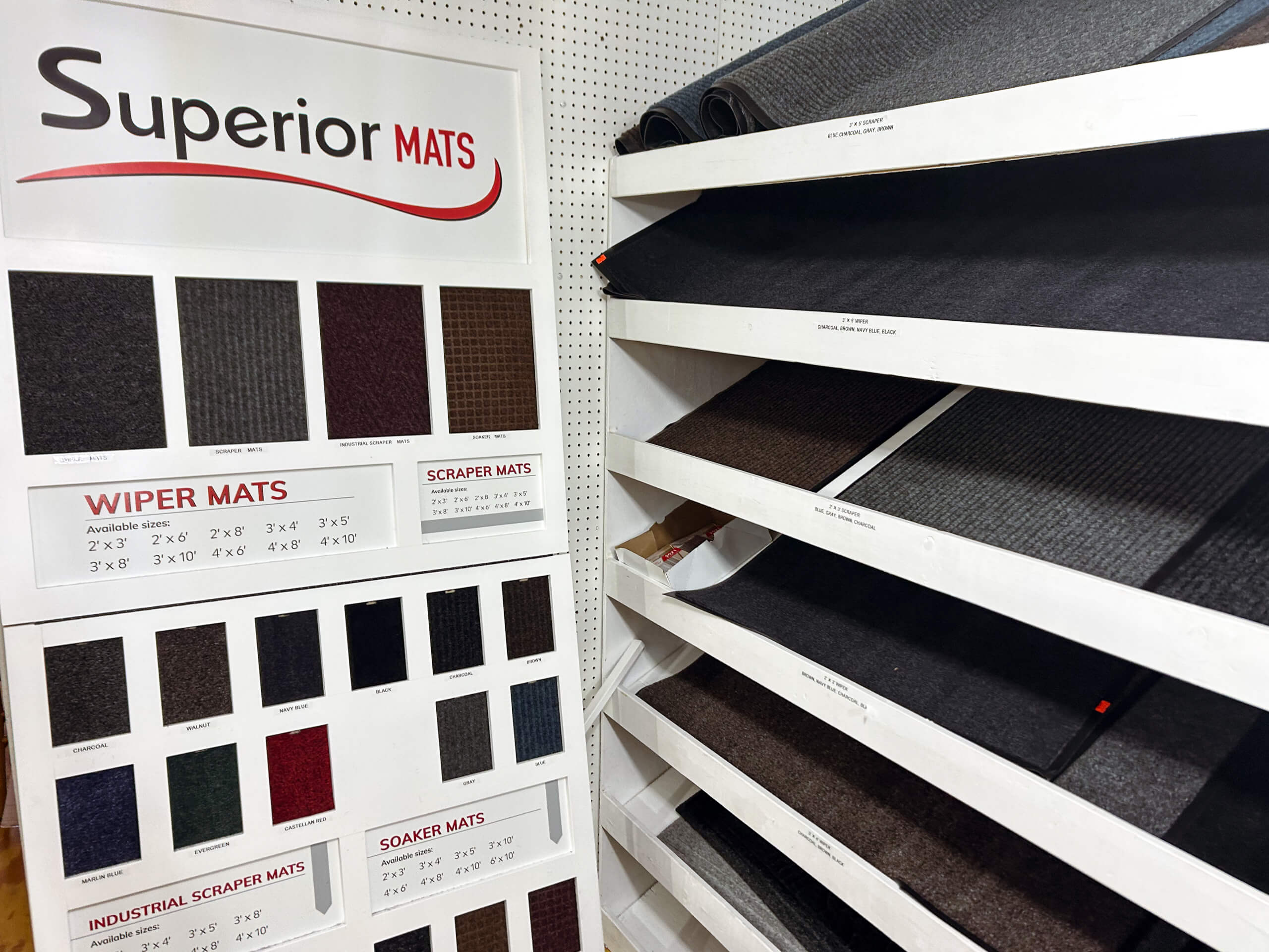 Miller's Country Store Grabill IN Display of various wiper and scraper mats in different colors and sizes, with labeled samples on a board and several rolled mats on shelves.
