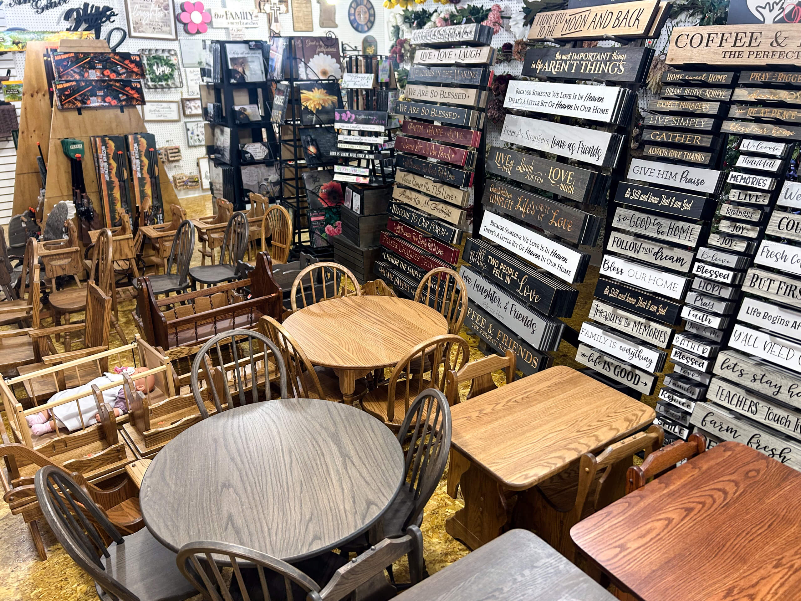 Miller's Country Store Grabill IN A shop displays multiple wooden tables, chairs, and benches, with a wall covered in decorative wooden signs featuring various sayings and inspirational messages.