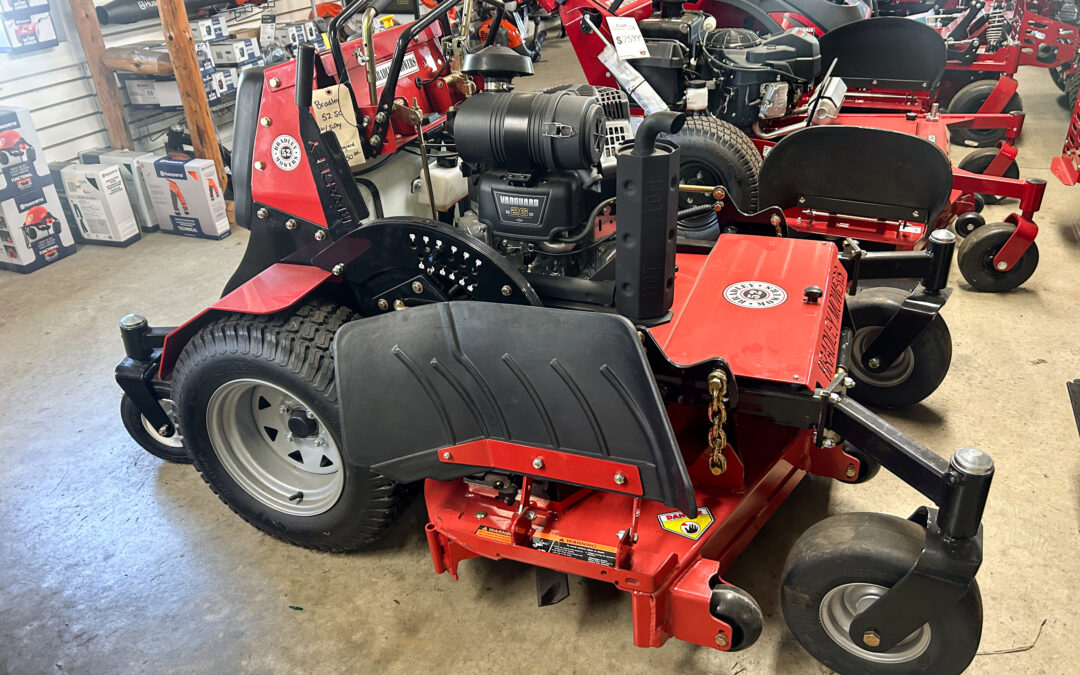 Miller's Sales & Service Centerville, MI Red commercial zero-turn lawn mower displayed indoors among other mowers and equipment, showing the engine, wheels, and control area.