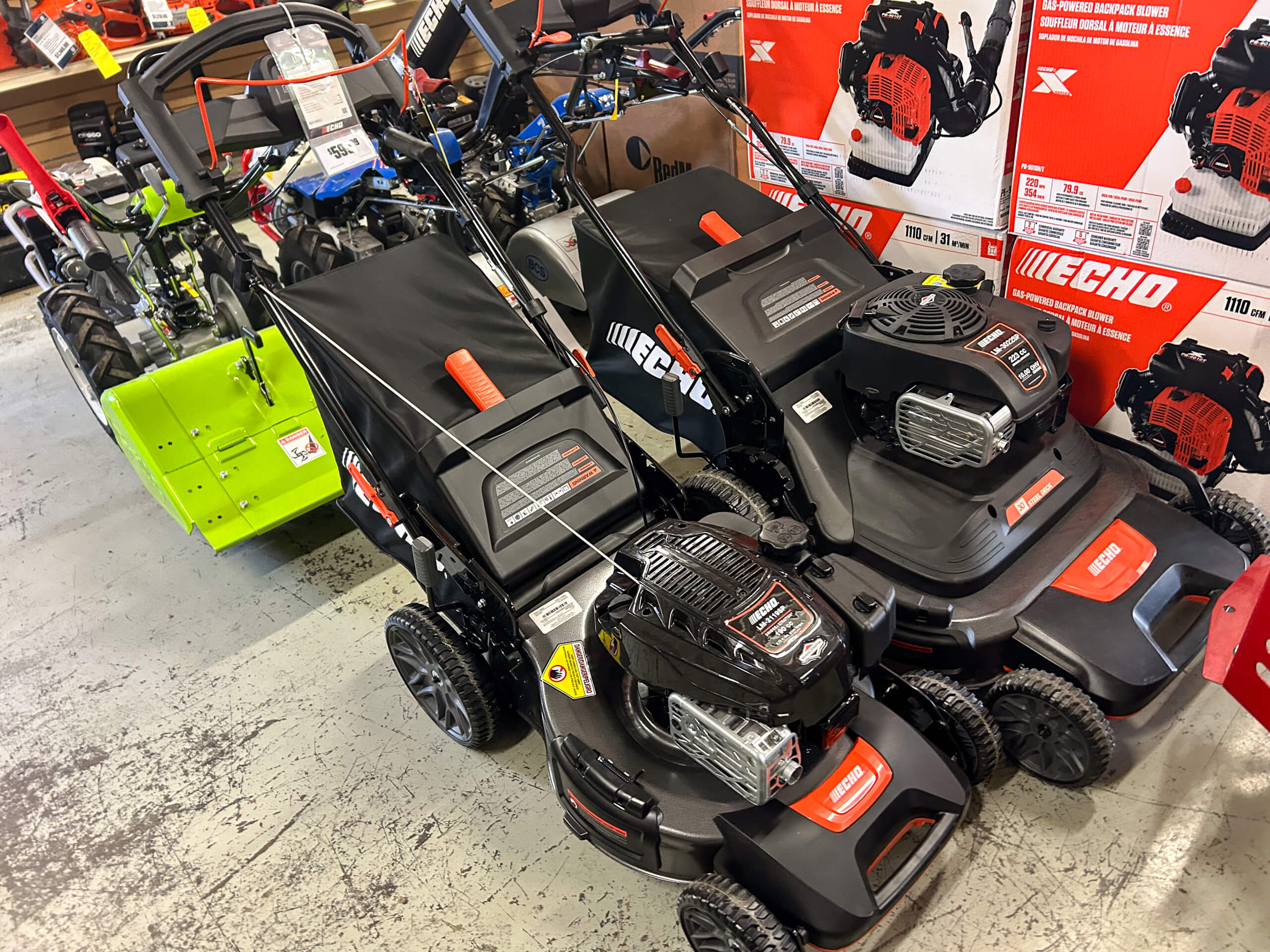 AK Small Engines Versailles, MO Several black and red lawn mowers are displayed on a store floor near boxes and other equipment.