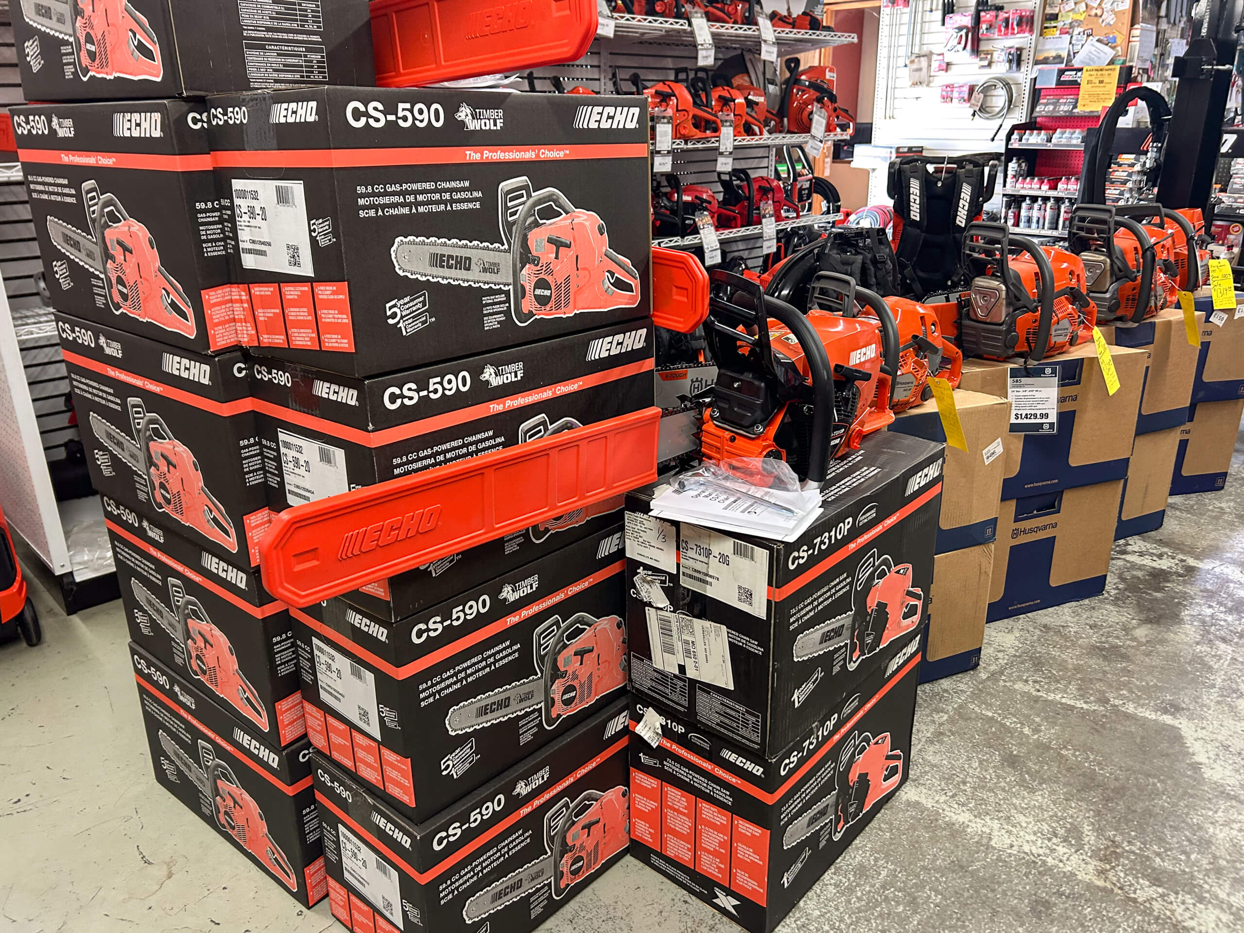 AK Small Engines Versailles, MO Stacks of Echo CS-590 chainsaw boxes and assembled chainsaws are displayed on the floor of a hardware store.