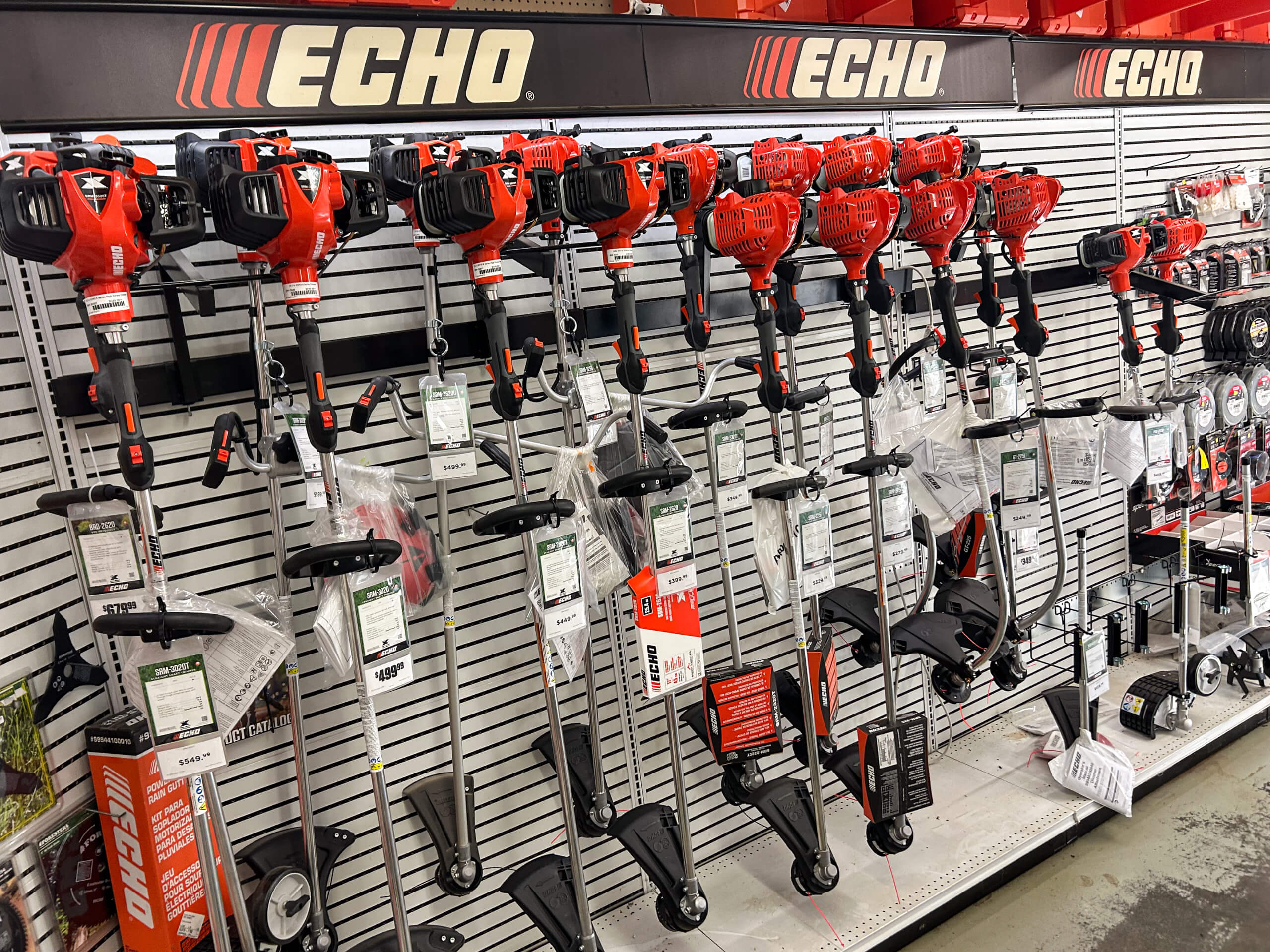 AK Small Engines Versailles, MO A row of Echo brand string trimmers and power tools are displayed on a store wall, with price tags and accessories hanging below.