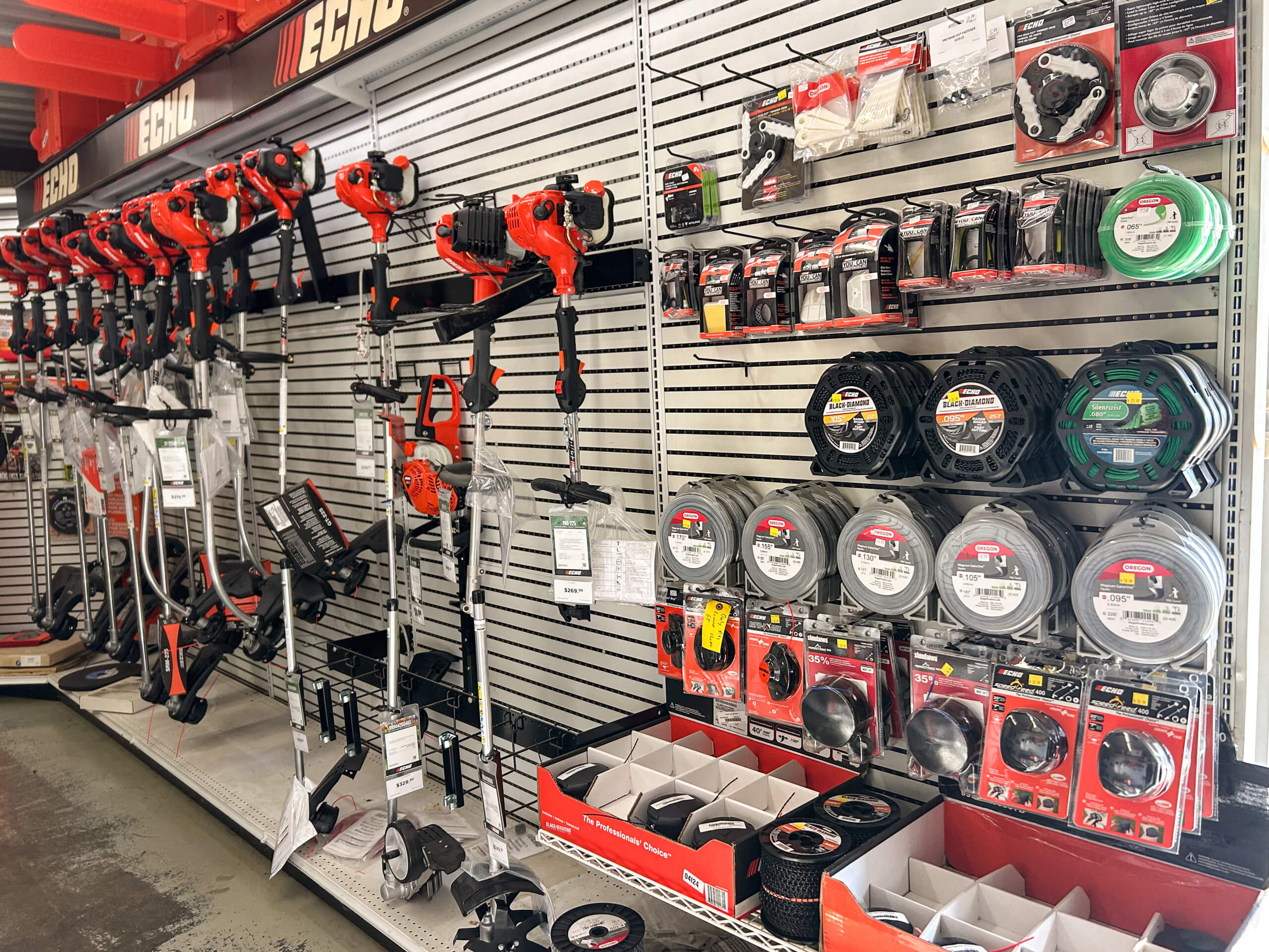 AK Small Engines Versailles, MO Shelves in a hardware store display various trimmers, power tools, replacement parts, and accessories, all organized and labeled for sale.