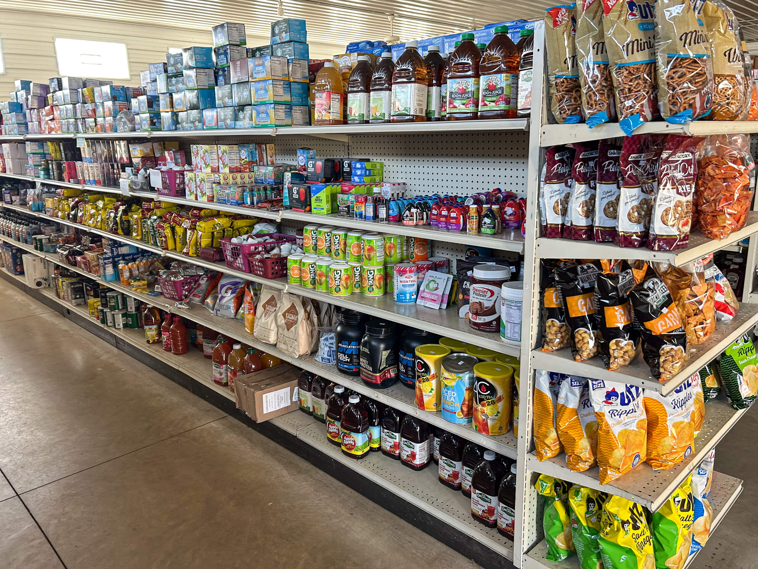 Sunrise Discount Grocery Store Colon MI Grocery store aisle with shelves stocked with beverages, canned goods, chips, and snacks under fluorescent lighting.