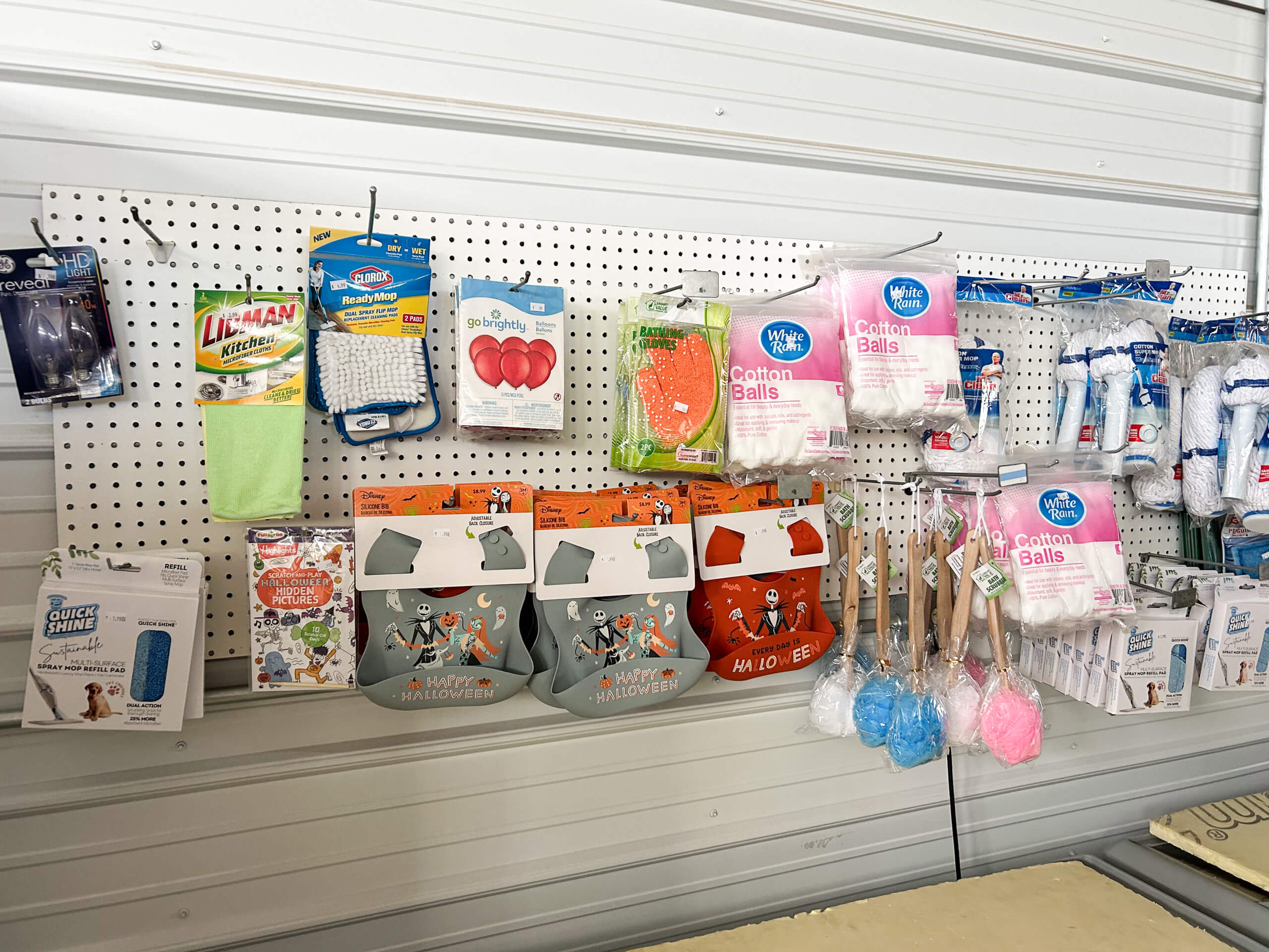Sunrise Discount Grocery Store Colon MI A pegboard wall displays cleaning sponges, Halloween-themed treat bags, cotton balls, shower loofahs, scrub brushes, and various household supplies in packaging.