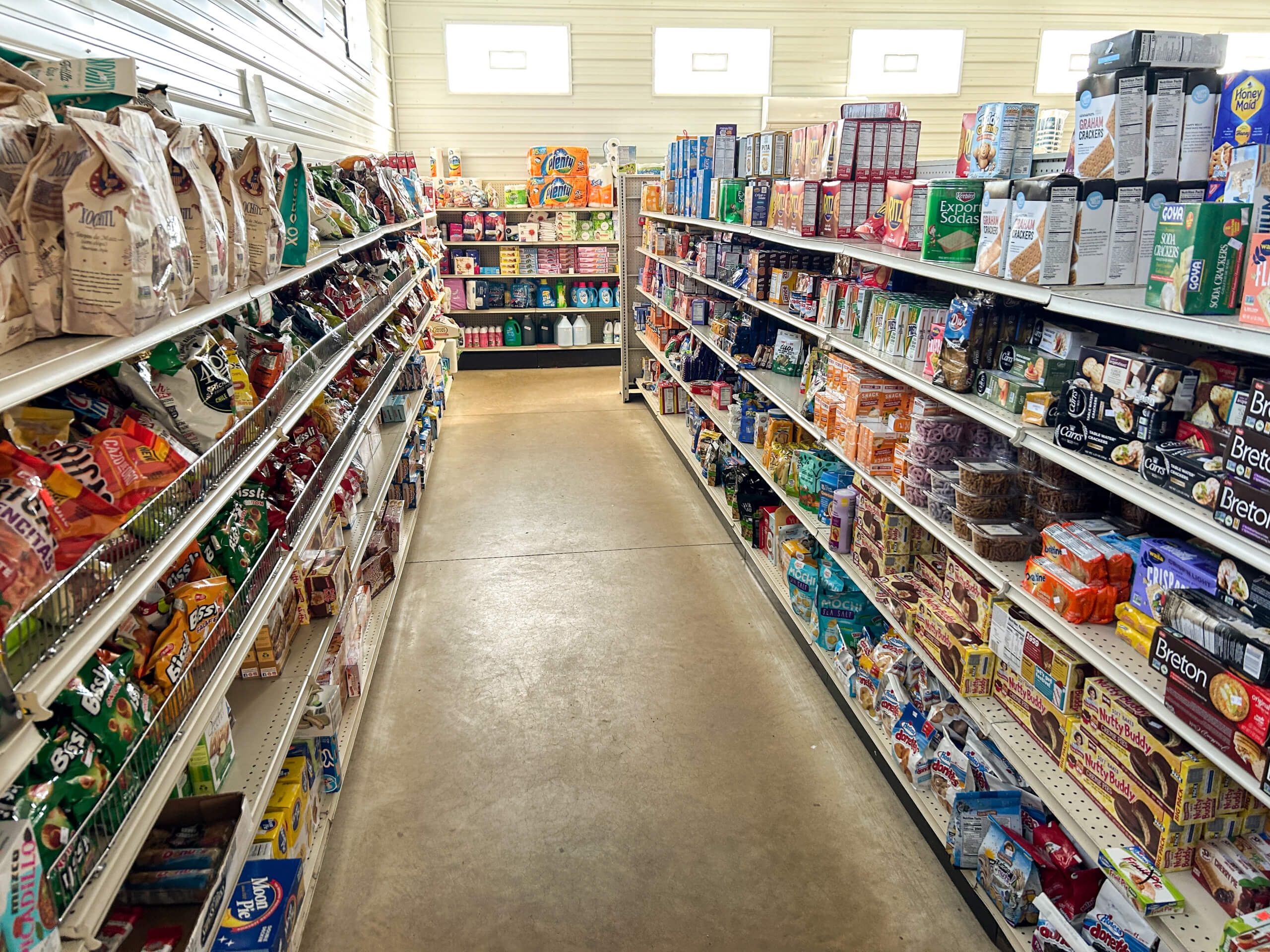 Sunrise Discount Grocery Store Colon MI A grocery store aisle with shelves stocked with various packaged food items, snacks, and household products on both sides.