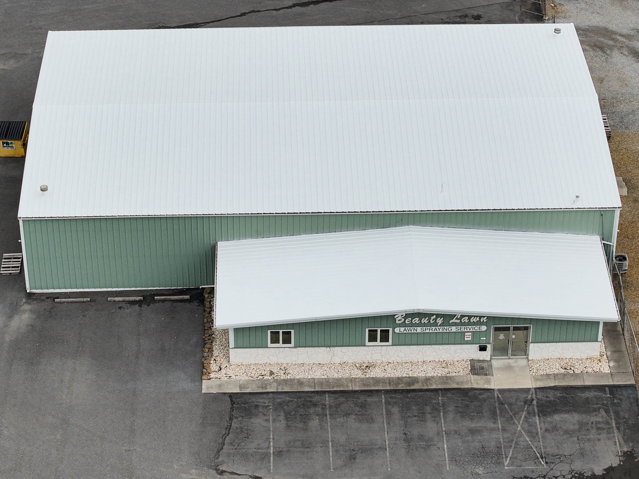 Winding Road Roofing After Restoration Hagerstown MD a green metal building with a white roof labeled "Beauty Lawn" and an adjacent larger warehouse structure on a paved lot.