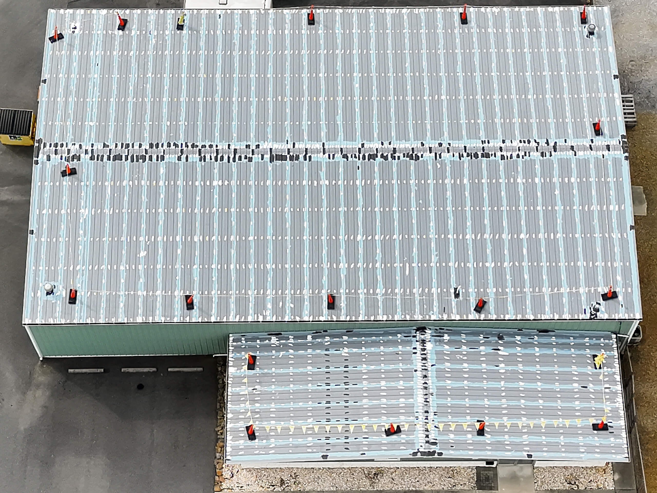 Winding Road Roofing After Restoration Hagerstown MD view of an industrial building with a large metal roof featuring evenly spaced red ventilation units and some scattered black markings.