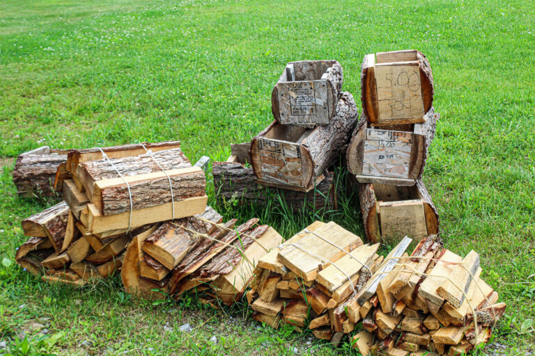 Coolspring Wood Products Mercer PA Stacks of firewood bundled with twine and wooden crates marked with prices are arranged on green grass.