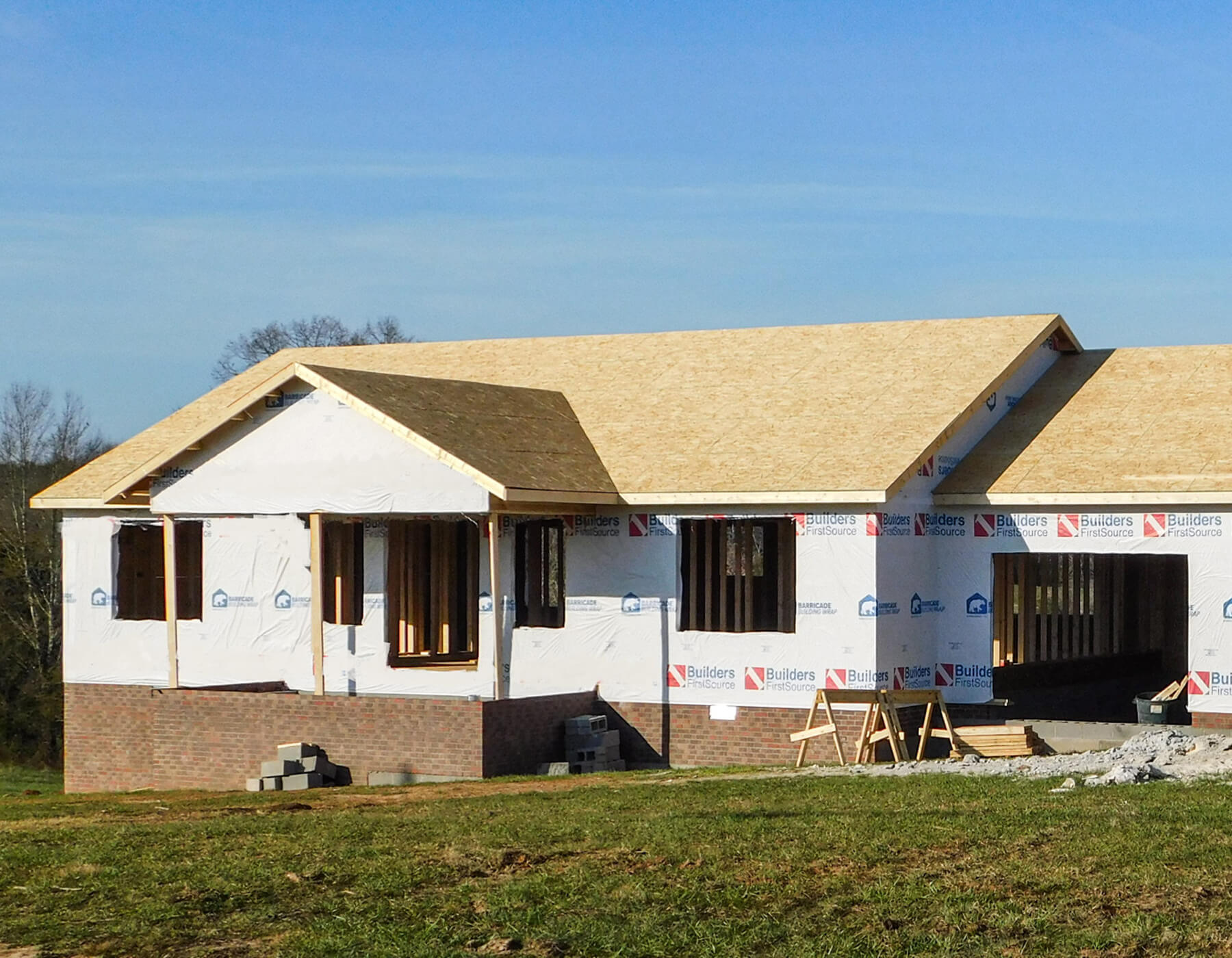 12.11.25 Mid-South Truss and Supply Gallery 2 A single-story house under construction with exposed plywood roof and house wrap on the exterior walls, situated on a grassy lot.