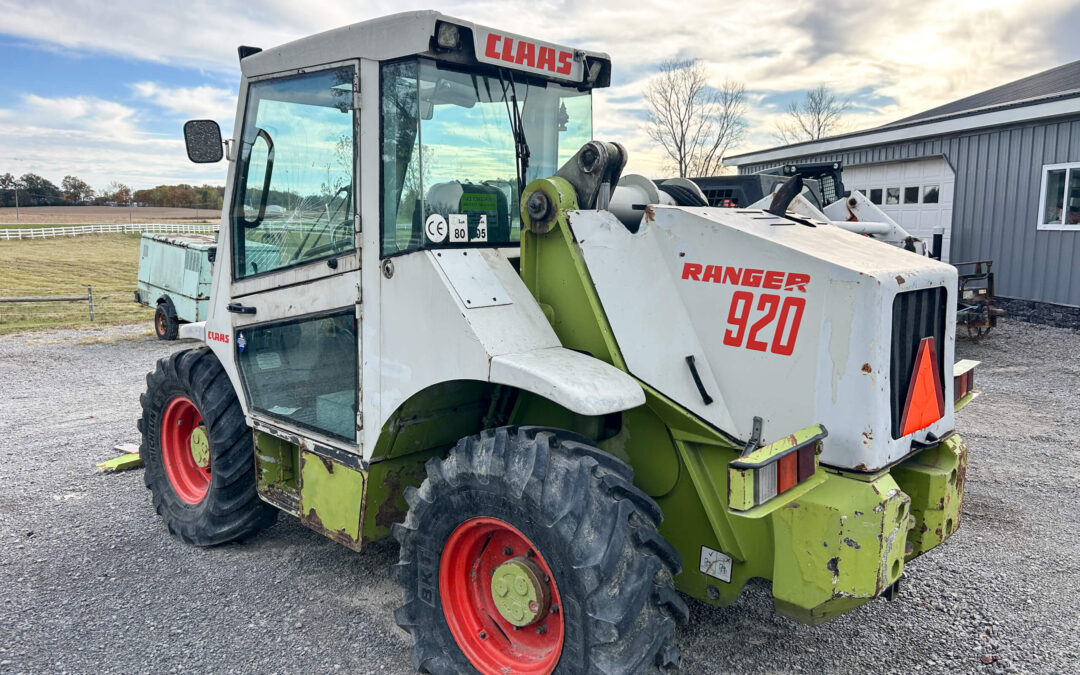 Troyer's Skidloader Repair Rushsylvania, OH A CLAAS Ranger 920 wheel loader with red rims is parked on gravel near a metal building and a grassy field.